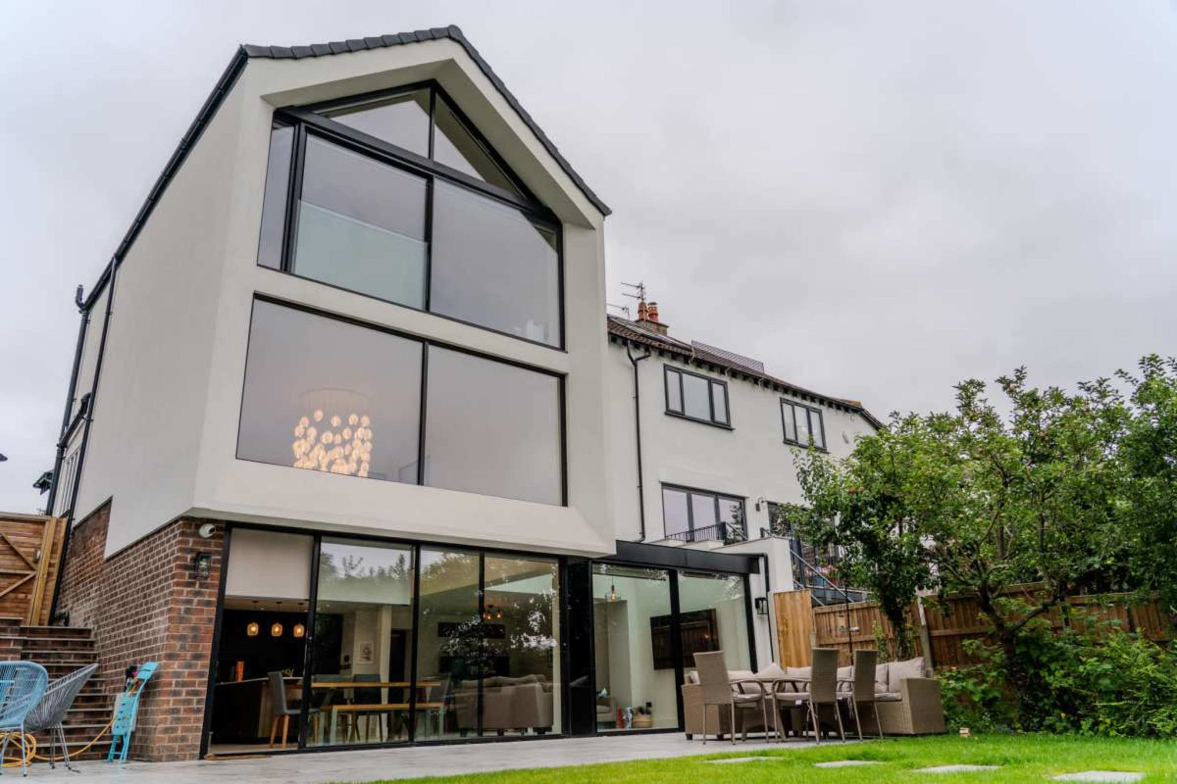 A modern two-story house with large windows and a glass sliding door opens to a neatly maintained garden area.