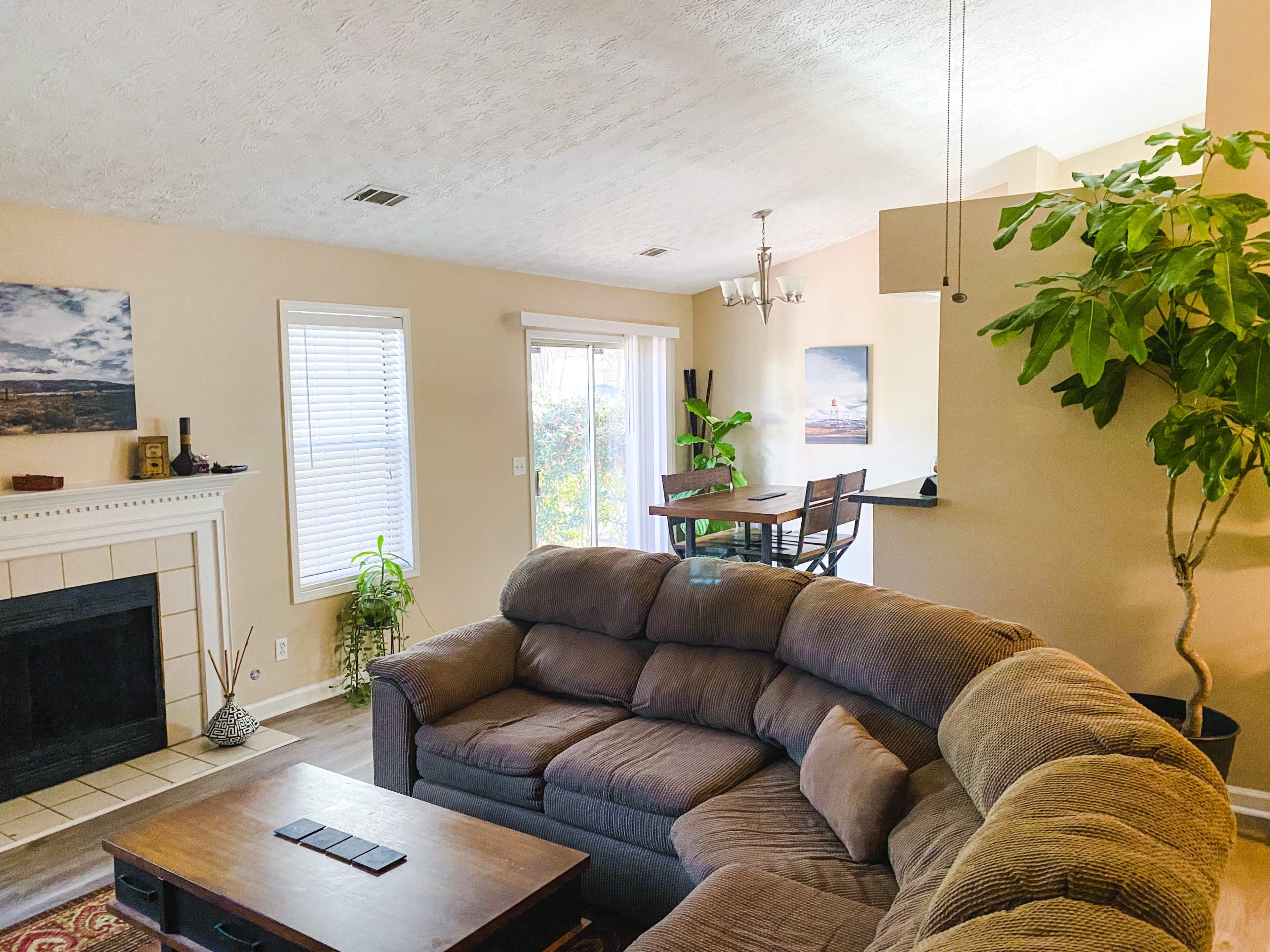 The image shows a living room with a large sectional sofa, a coffee table, a fireplace, and a dining area visible in the background.