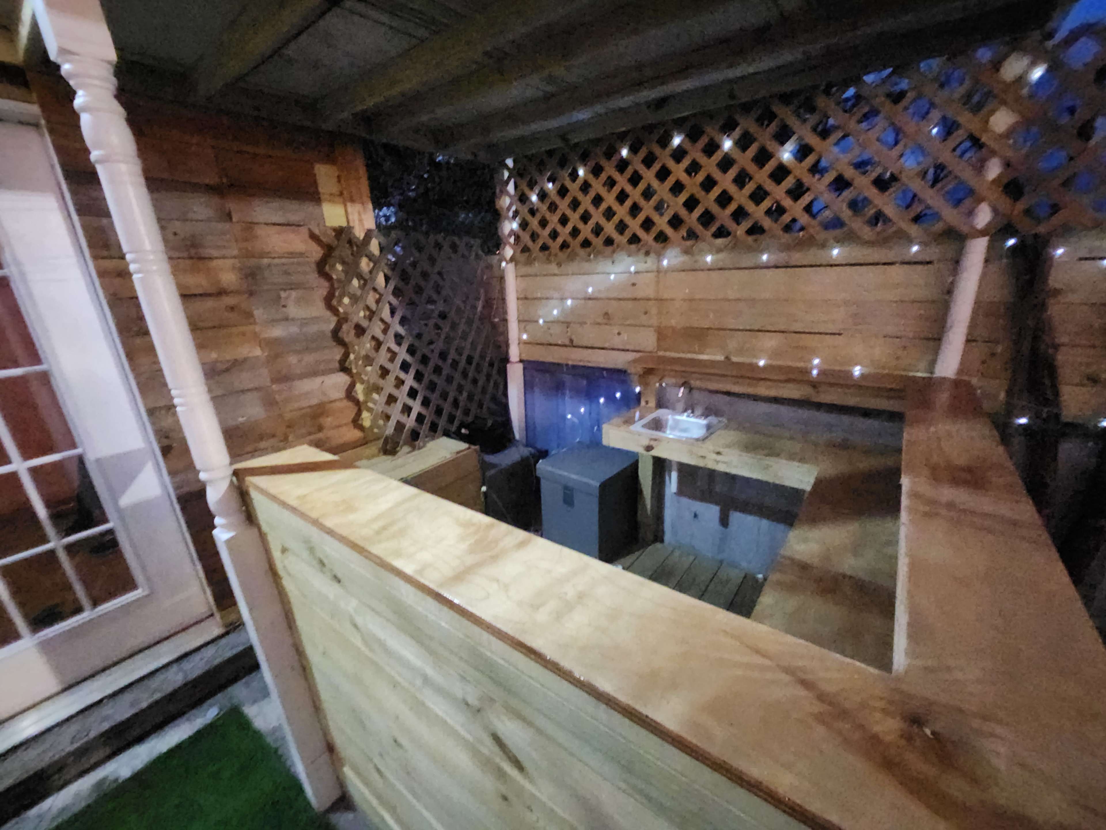 A wooden outdoor bar area with a lattice backdrop and ambient lighting.
