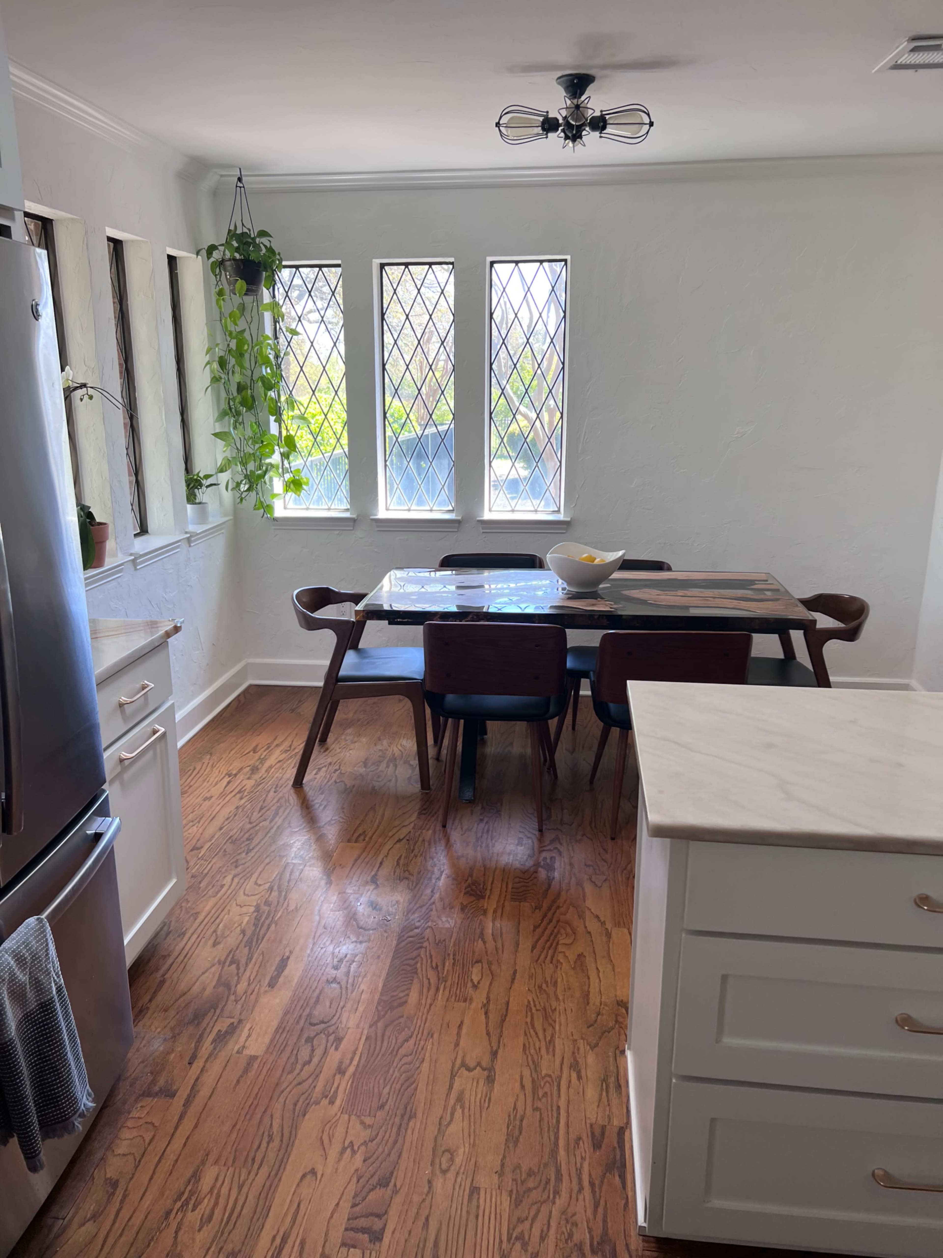 A bright kitchen with a dining table set for four, surrounded by large windows and wooden floors.