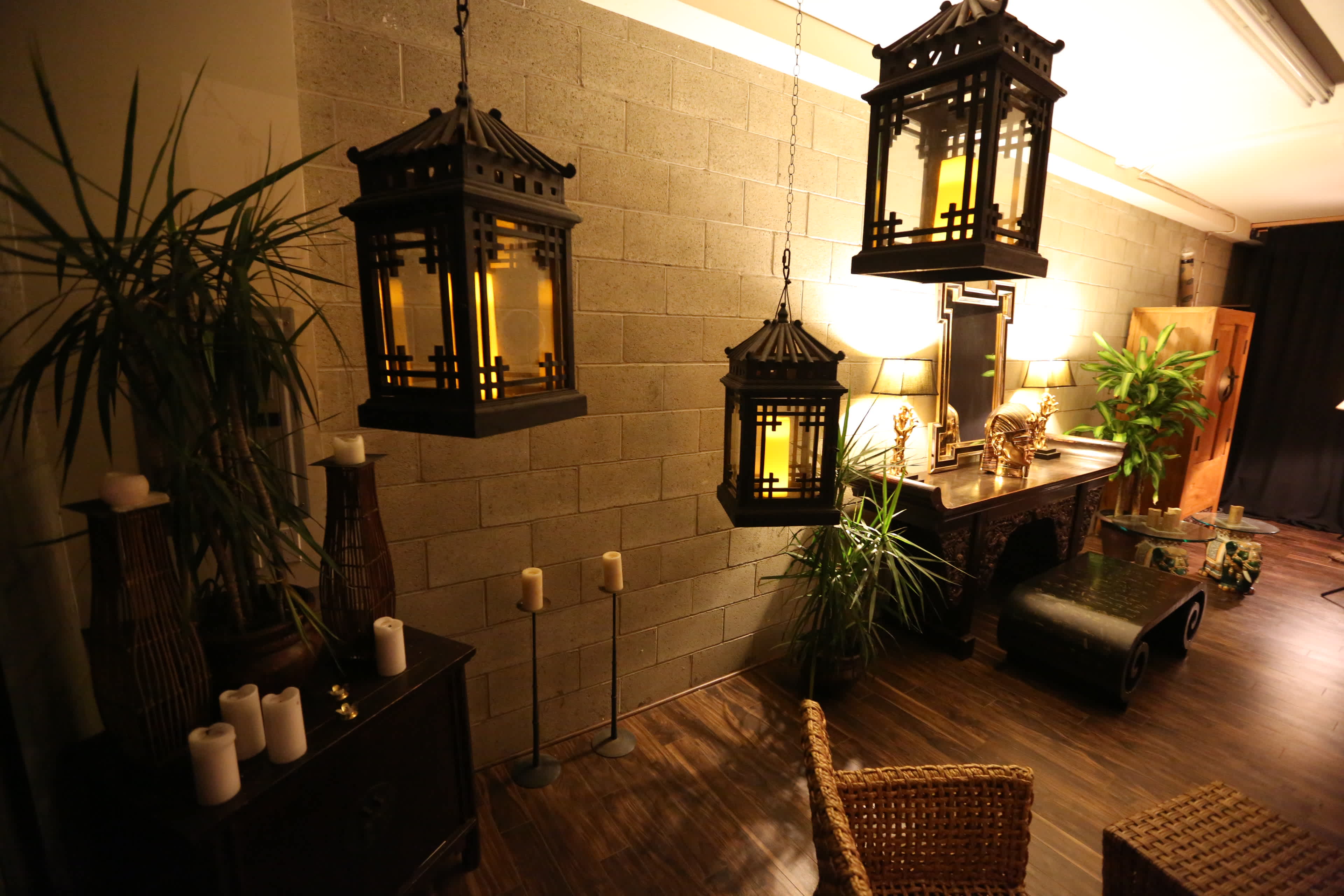 A well-decorated room with three hanging lanterns, potted plants, a wooden table, and a seating area.