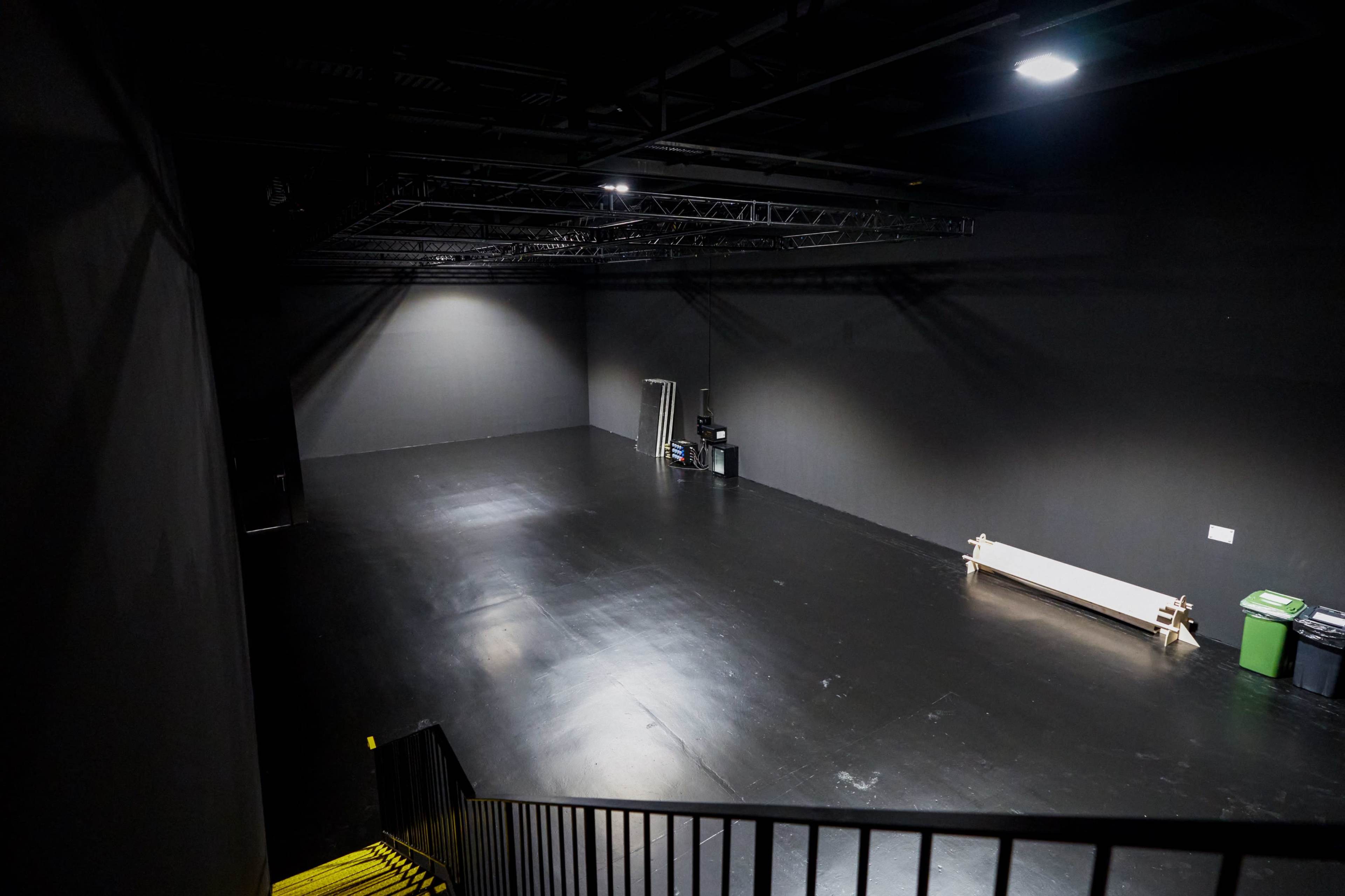 The image shows a spacious, dimly lit studio with a smooth black floor, a bench along one wall, and various equipment staged in one corner.