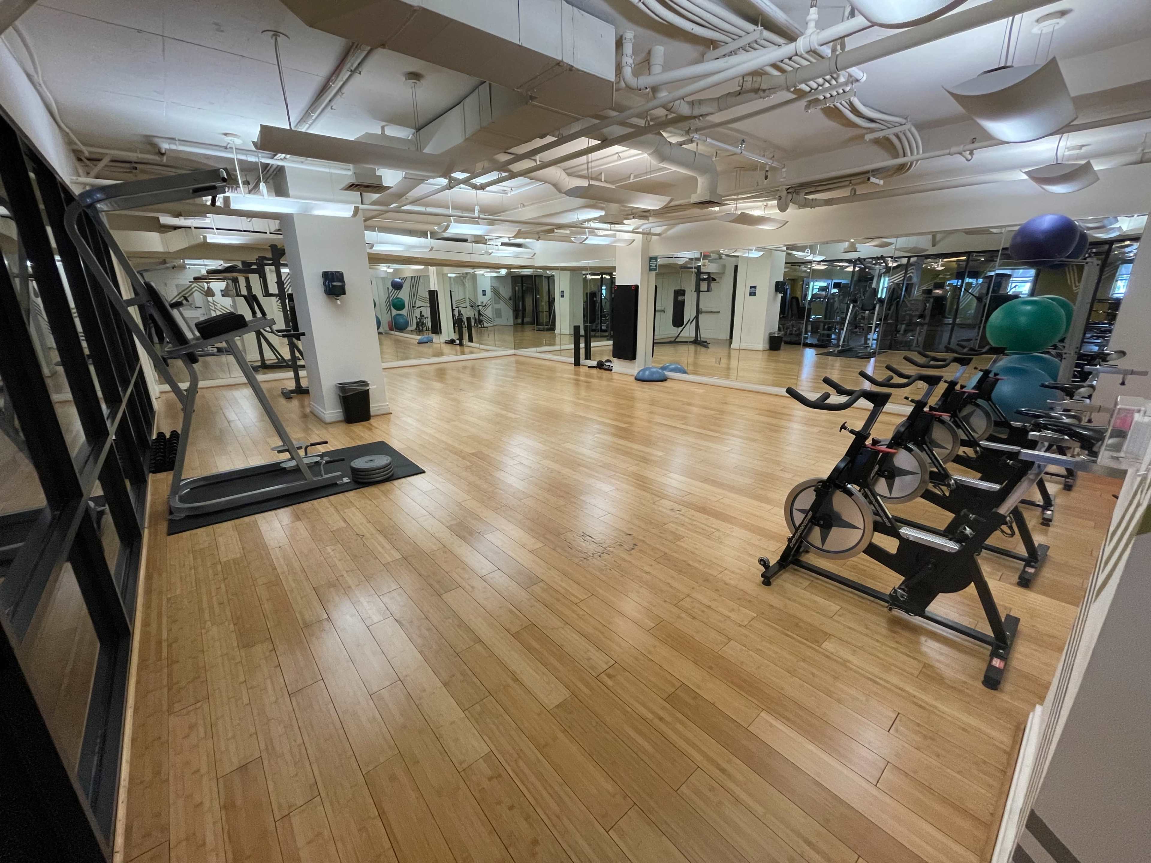A spacious, well-lit gym with exercise equipment, including stationary bikes and a treadmill, situated on a wooden floor.