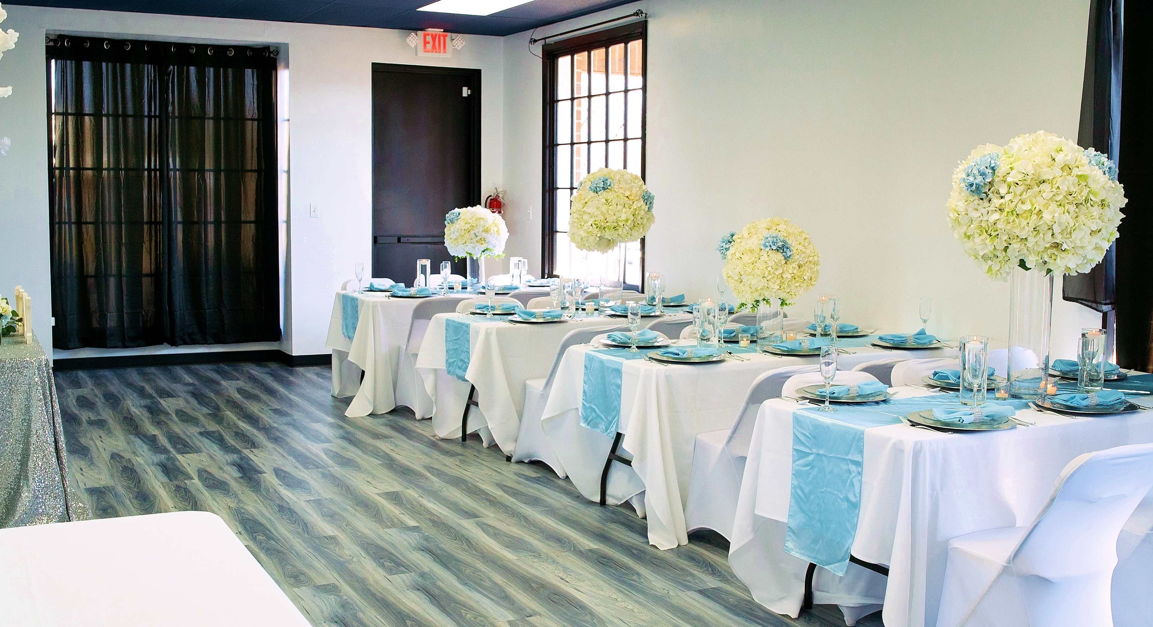 A elegantly set dining area with white tablecloths, blue accents, and floral centerpieces, arranged for an event.