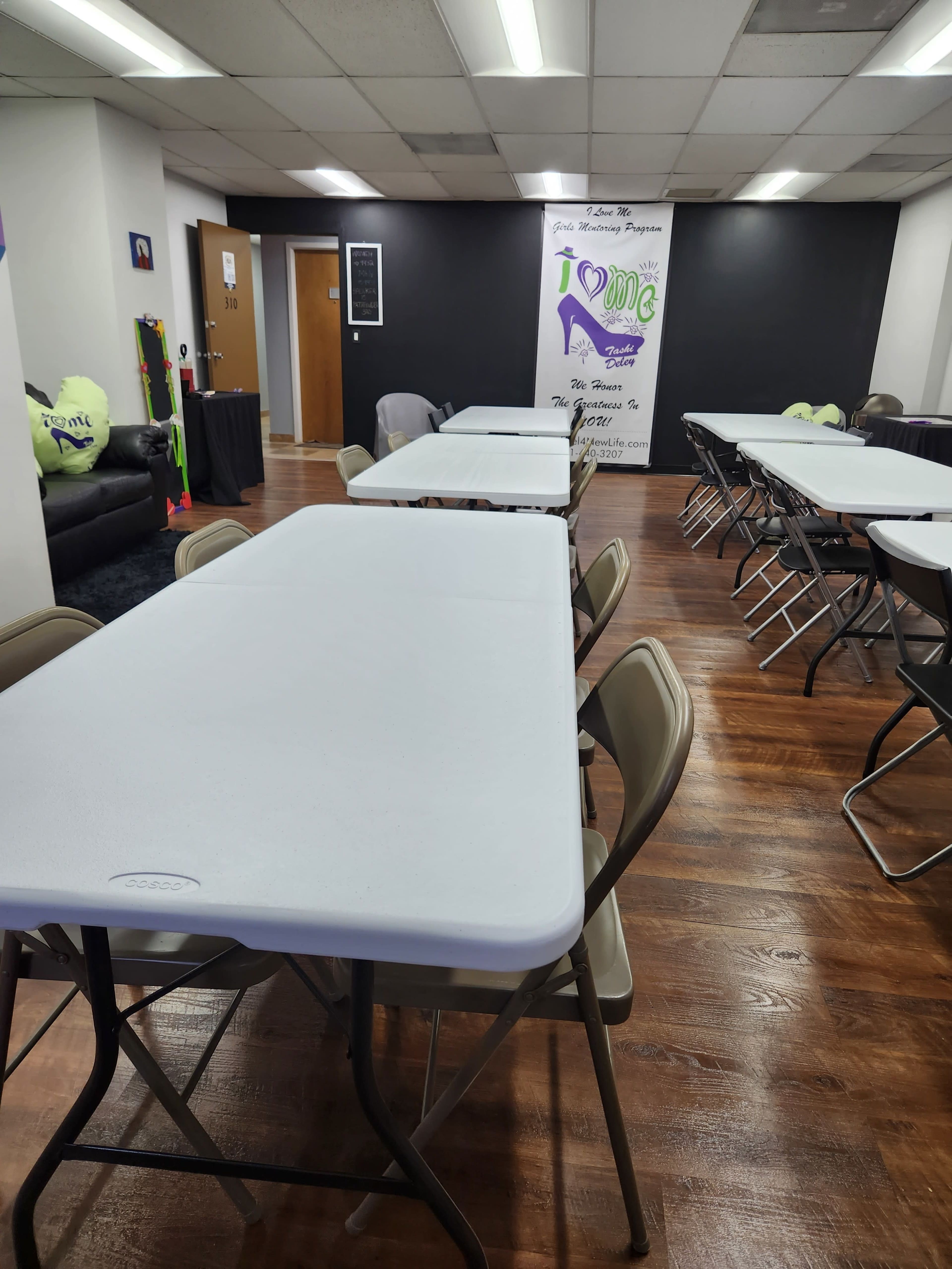 A spacious room with several folding tables and chairs arranged in rows, contrasting against a dark wall featuring a decorative banner.