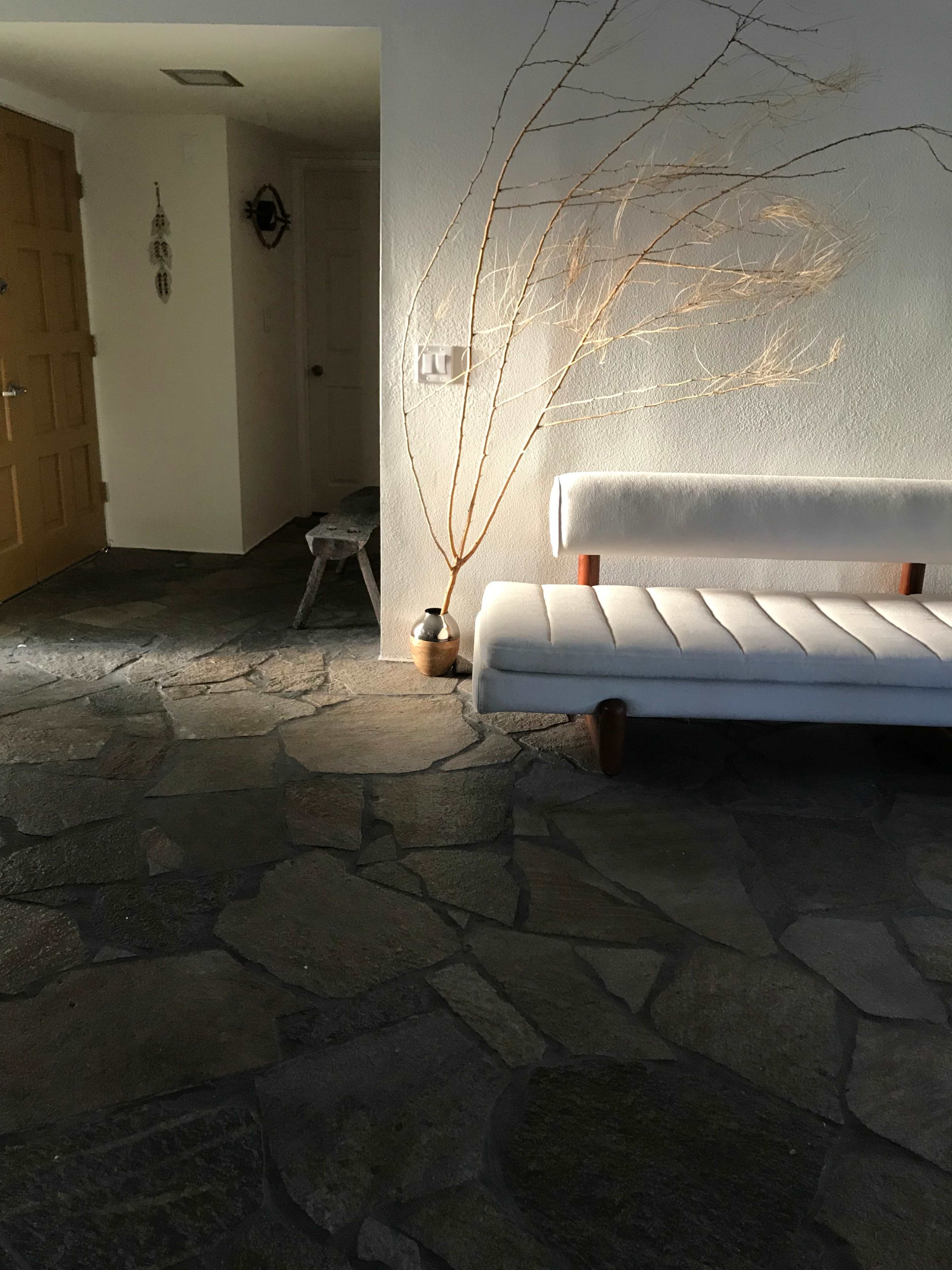 A minimalist interior features a stone floor, a white sofa, and a large decorative branch in a vase.