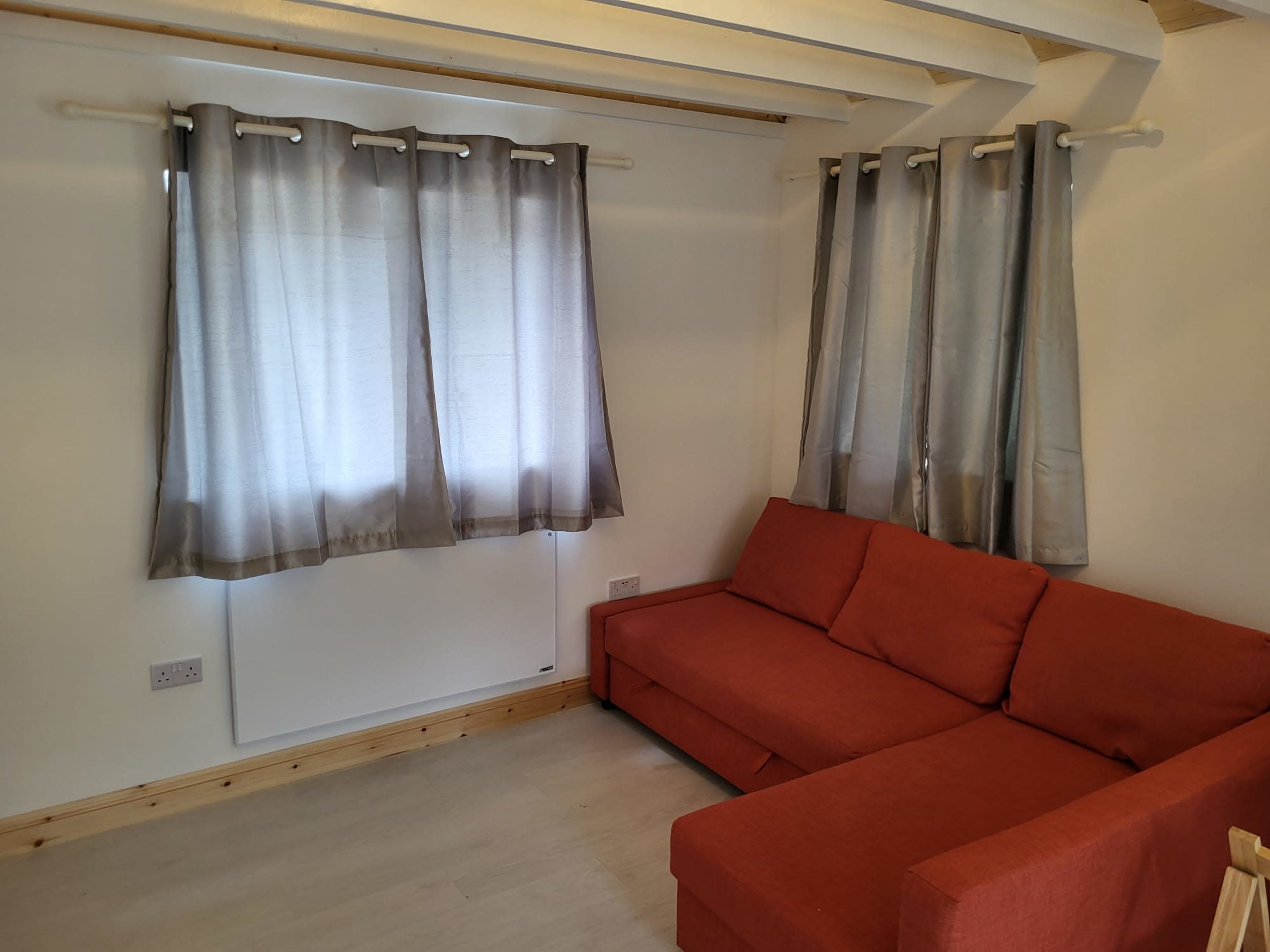 A minimalist living room featuring a red sofa and large curtains covering a window.