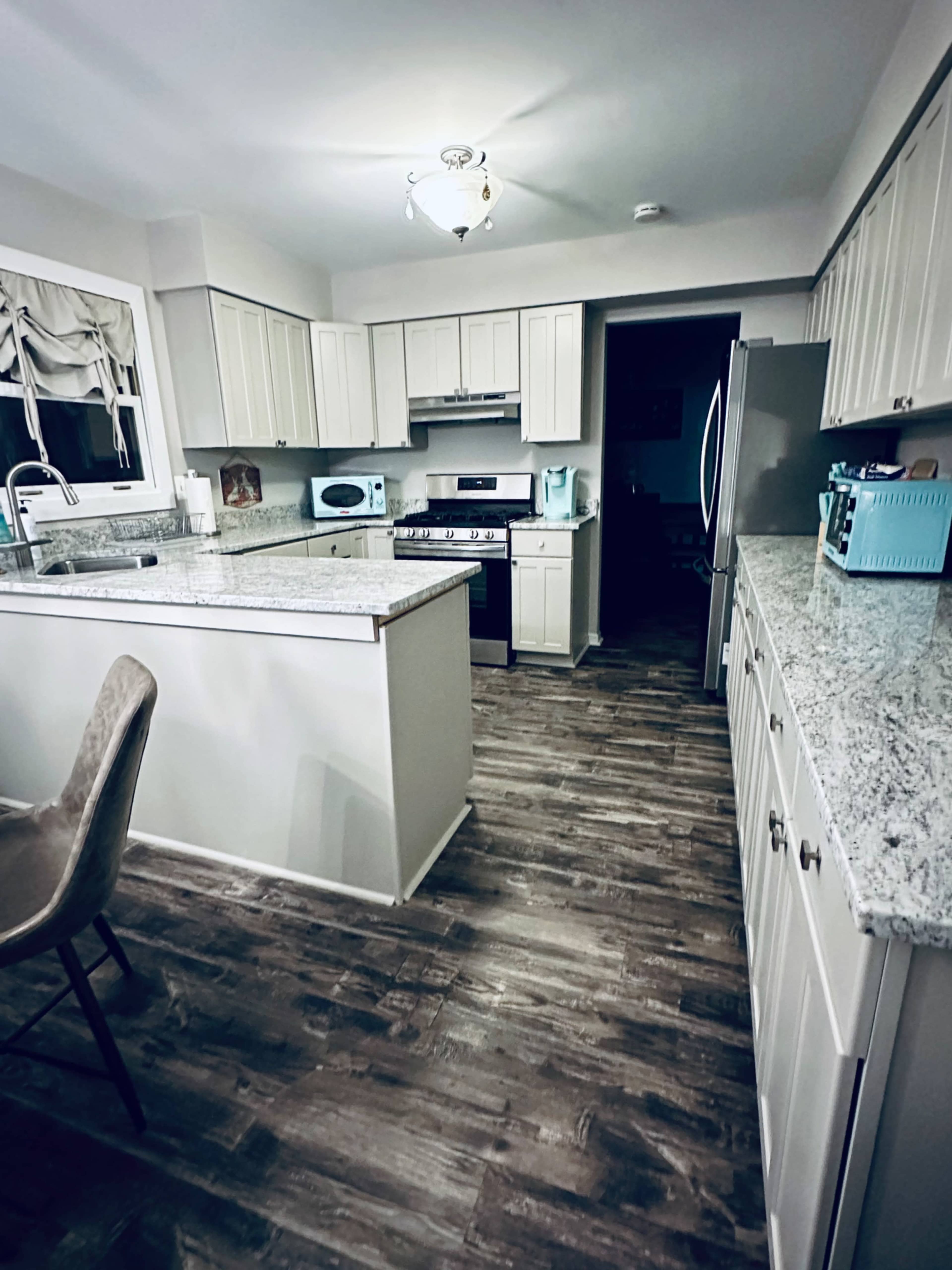 A well-lit kitchen features granite countertops, white cabinetry, and modern appliances, with a dining chair visible on the left.