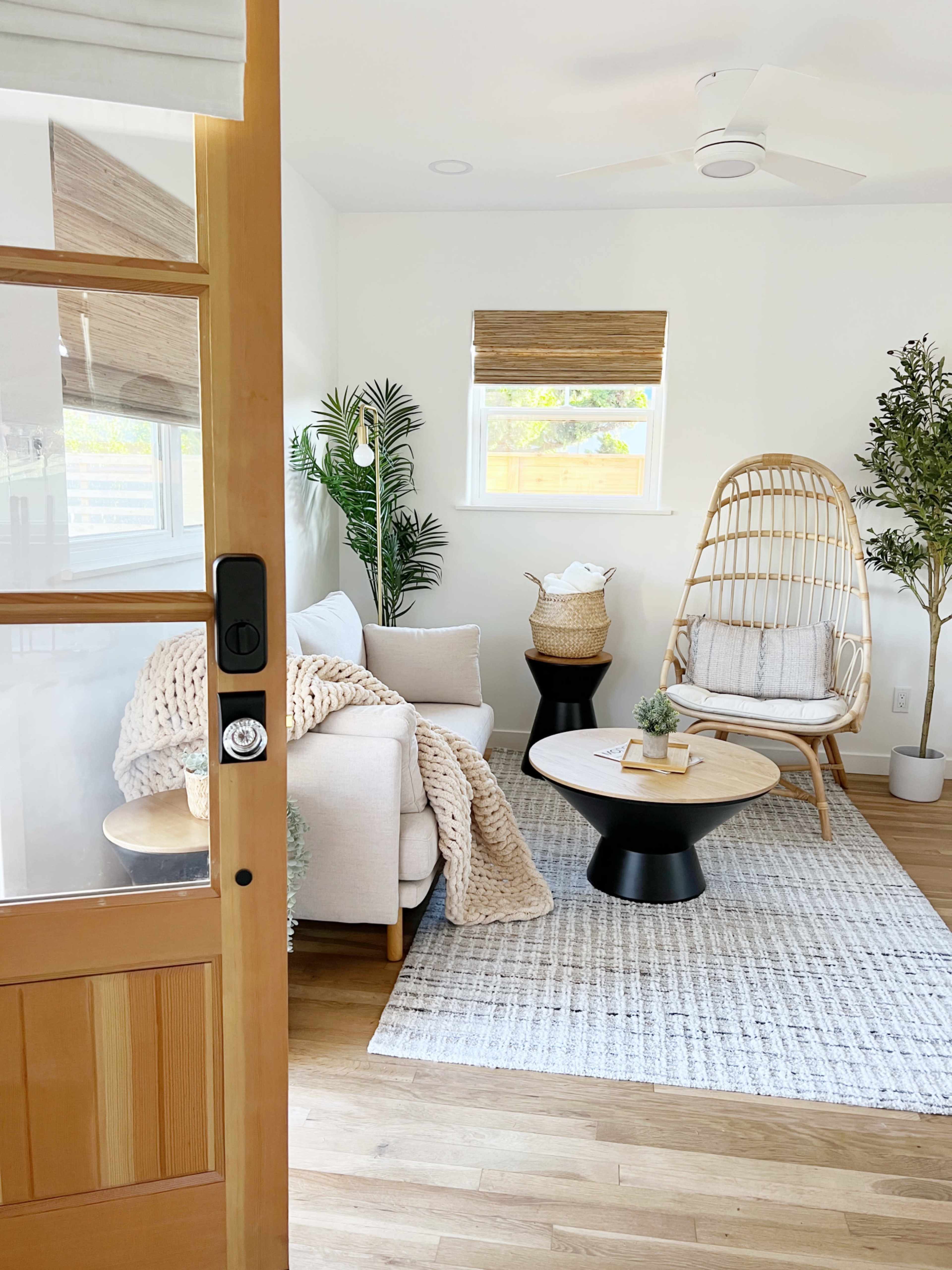 A cozy living room features a light-colored sofa, a rattan hanging chair, a round coffee table, and decorative plants on a neutral rug.