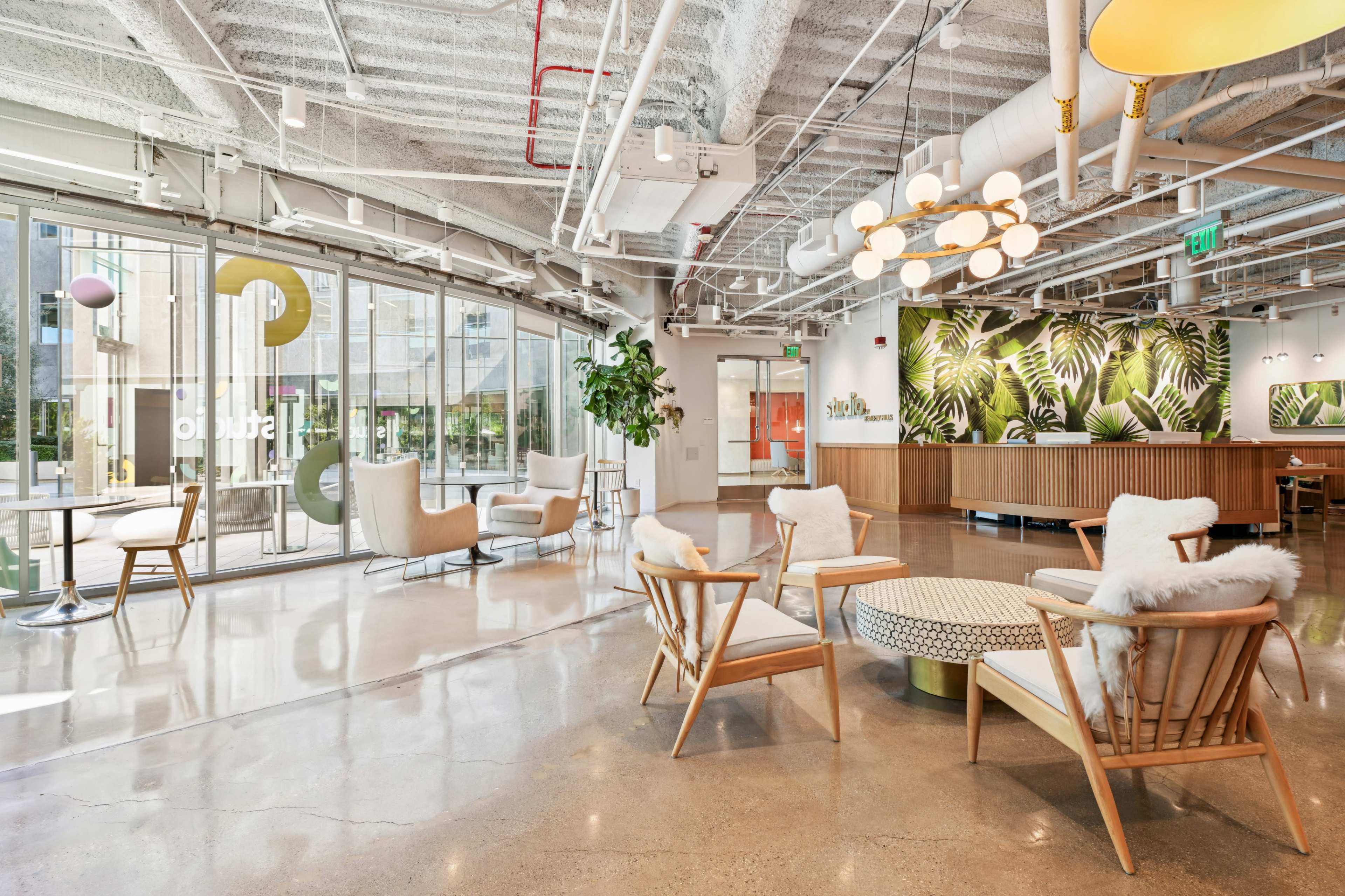 The image shows a modern interior space with wooden furniture, large windows, and a green plant wall.