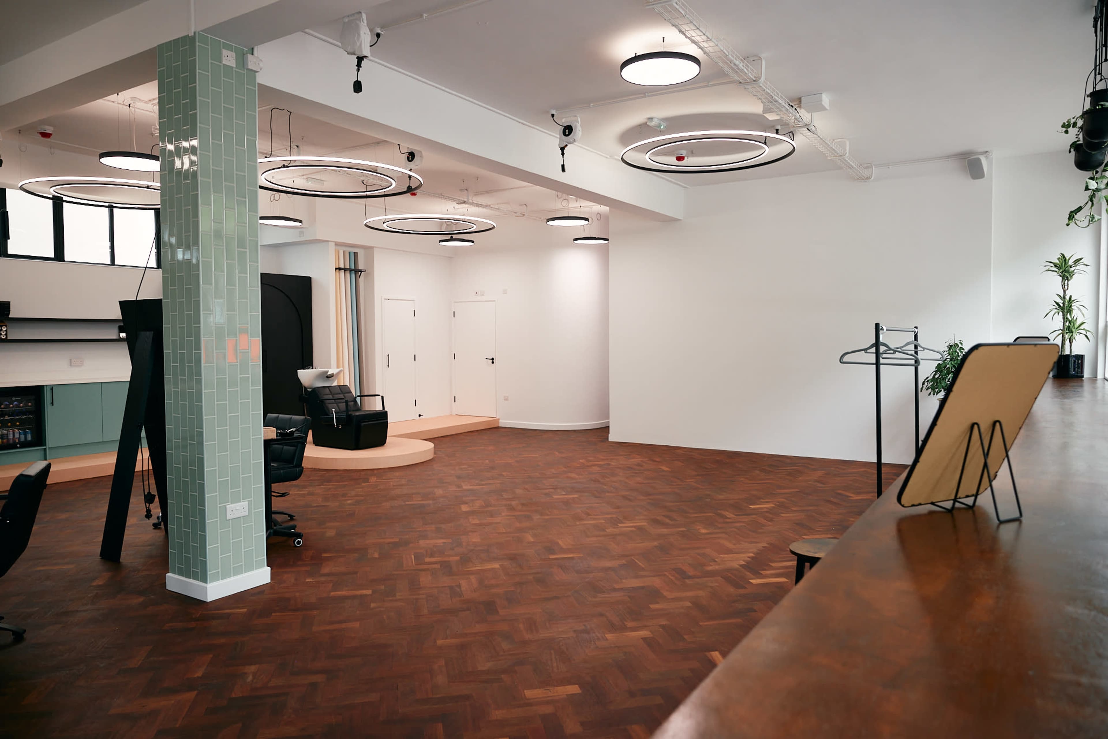 A spacious, modern room featuring herringbone wooden flooring, green tiled columns, and circular ceiling lights.