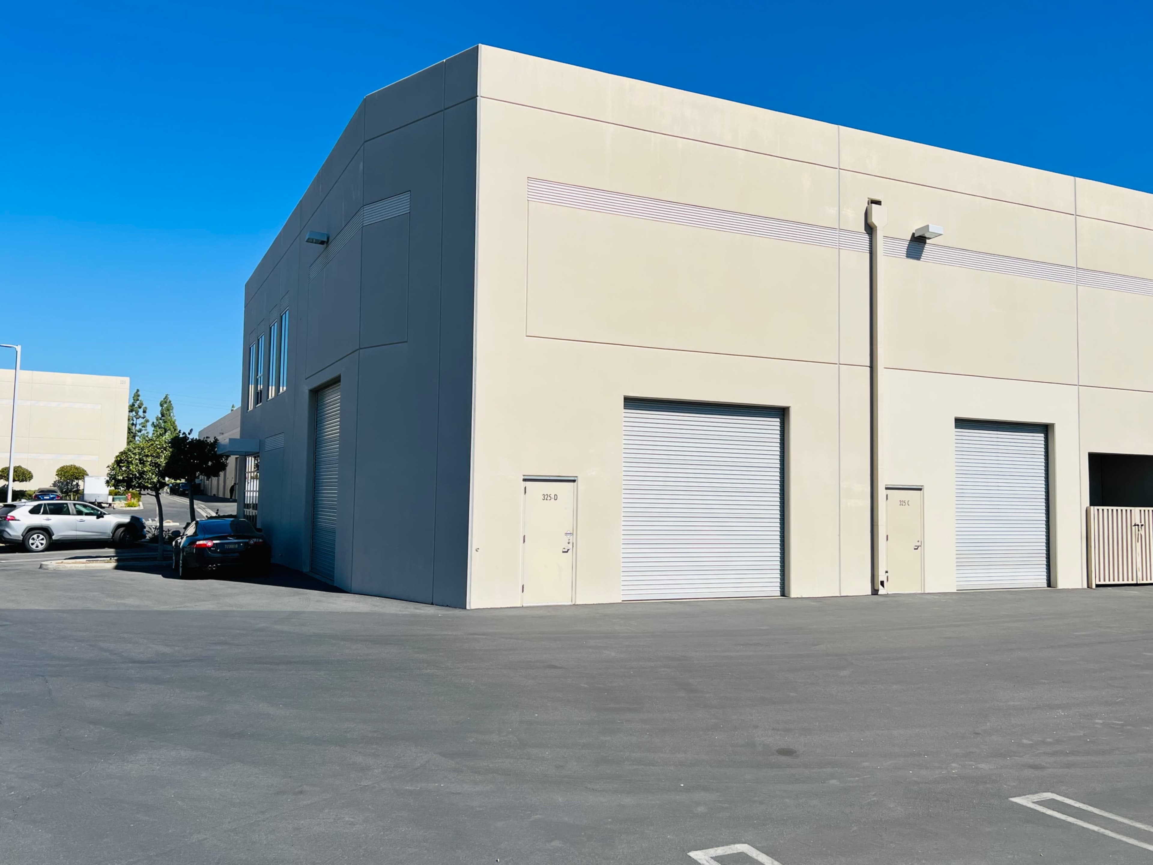 A light-colored industrial building features two roll-up doors and parked vehicles in the foreground.