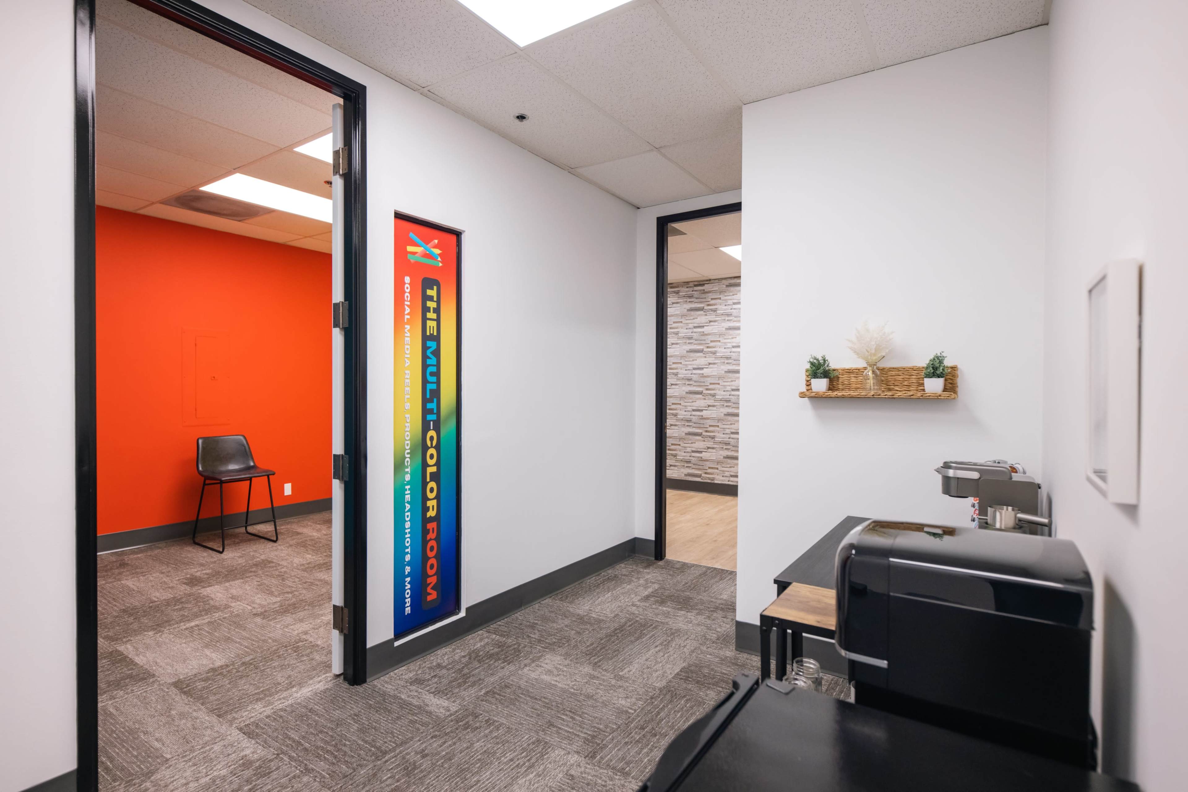 A hallway leads to a room with an orange wall, featuring a coffee station and decor on the opposite side.