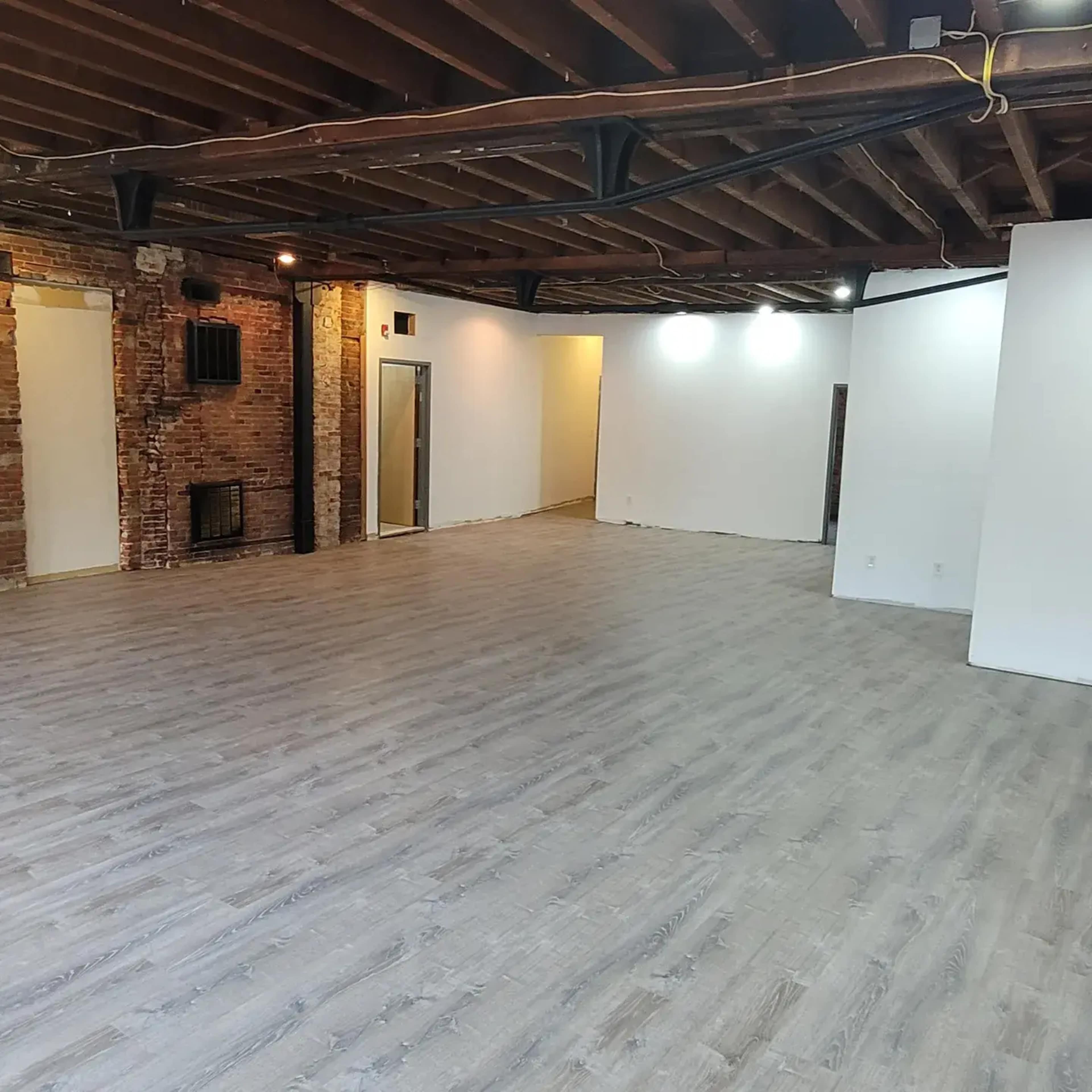 A large, empty room with wooden beams on the ceiling, brick walls, and a light-colored wooden floor.