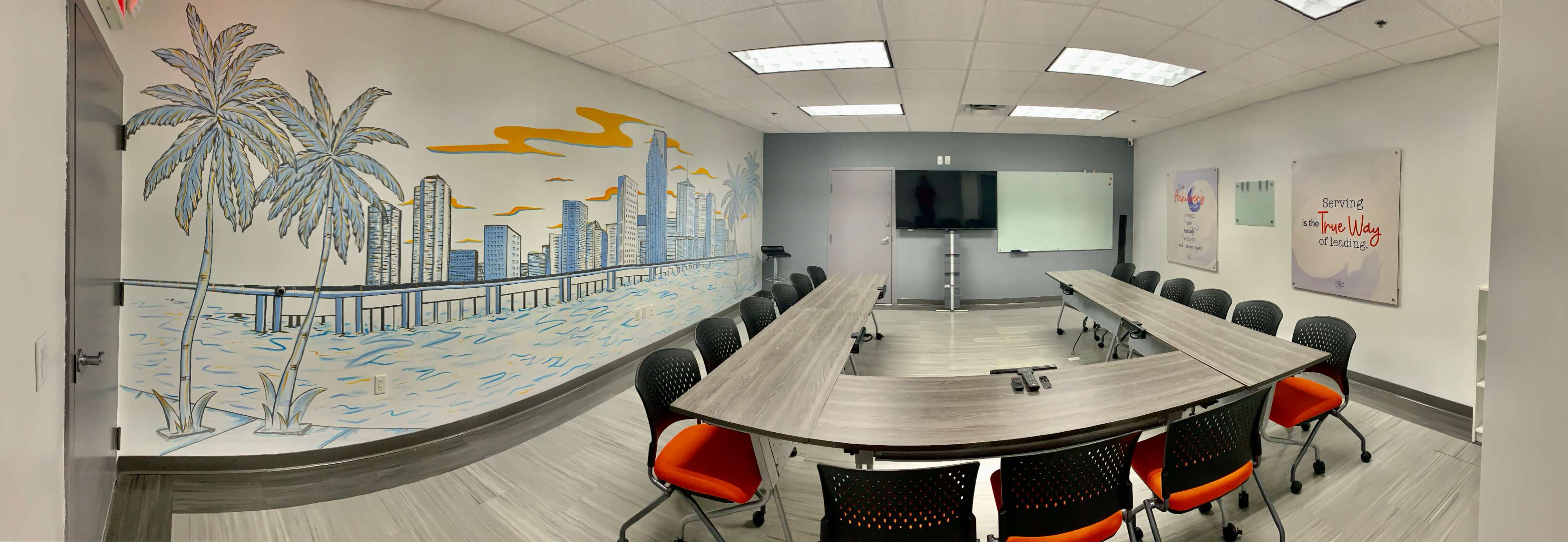 The image shows a modern conference room with a long table surrounded by black chairs, featuring a mural of a city skyline and palm trees on one wall.