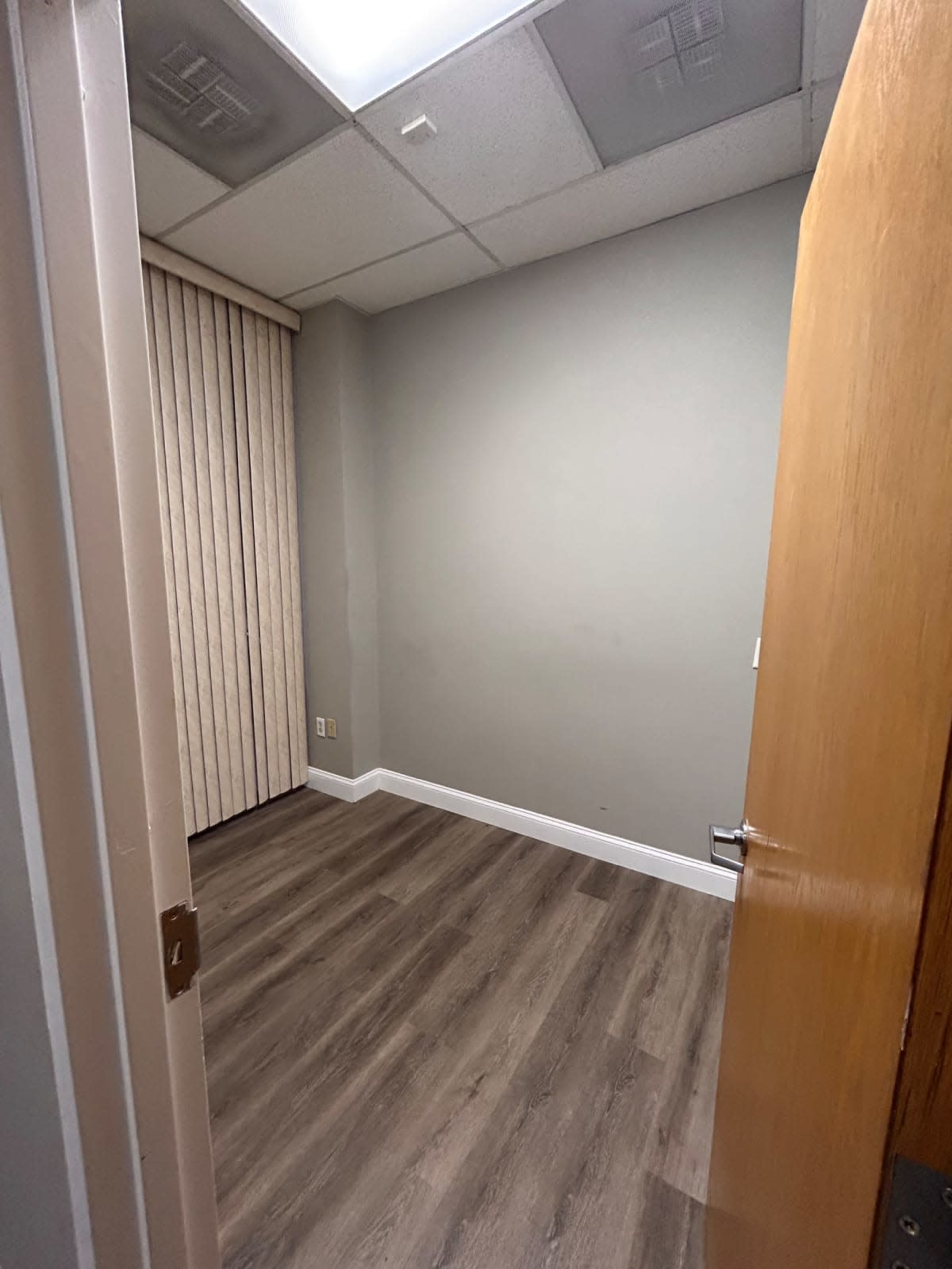 A small, sparsely furnished room with a door ajar, light gray walls, and laminate flooring.