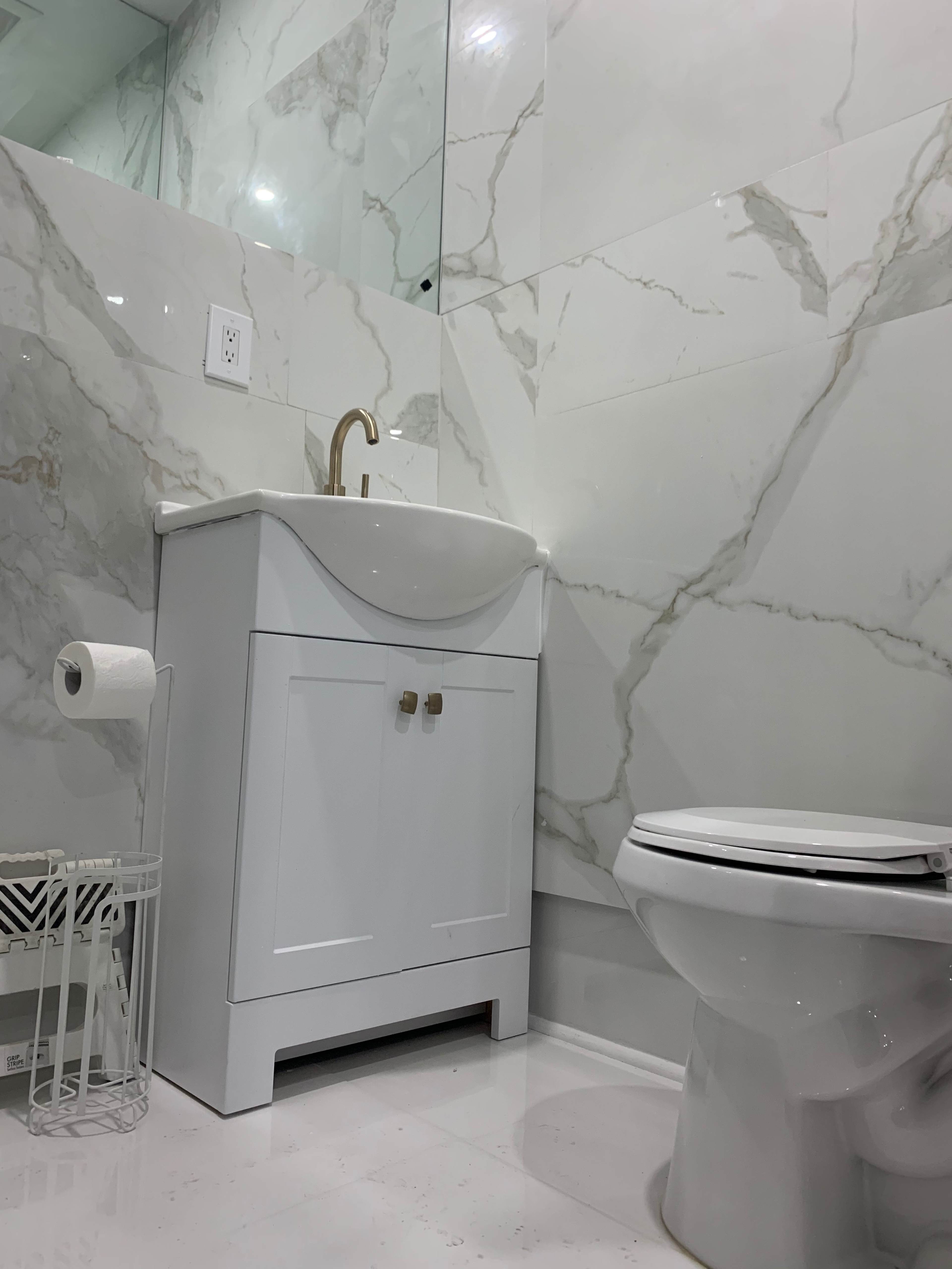 A modern bathroom features a white vanity with a sink, a toilet, and marble-patterned wall tiles.