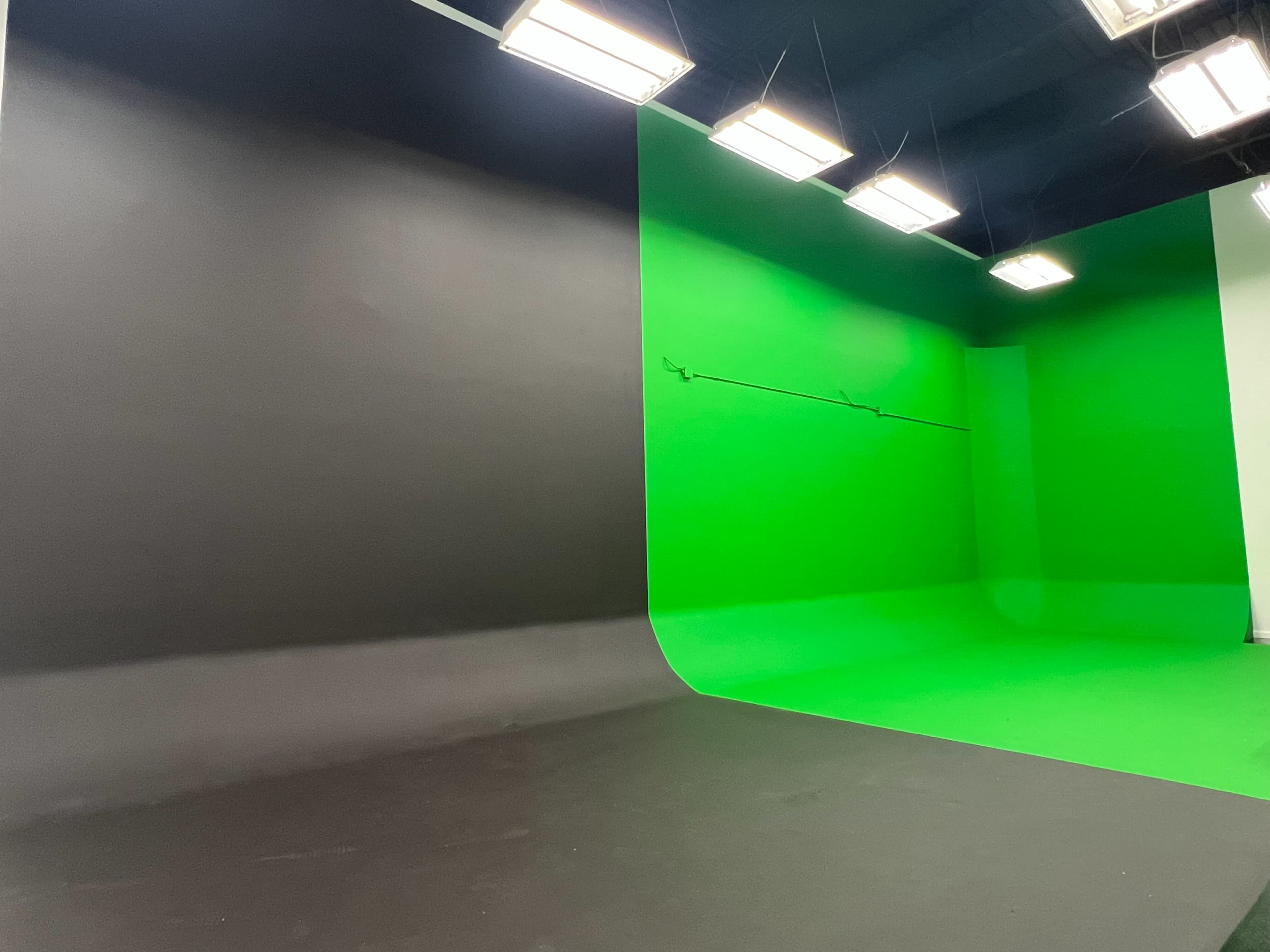 A film studio set with a black backdrop on one side and a green screen backdrop on the other, illuminated by overhead lights.