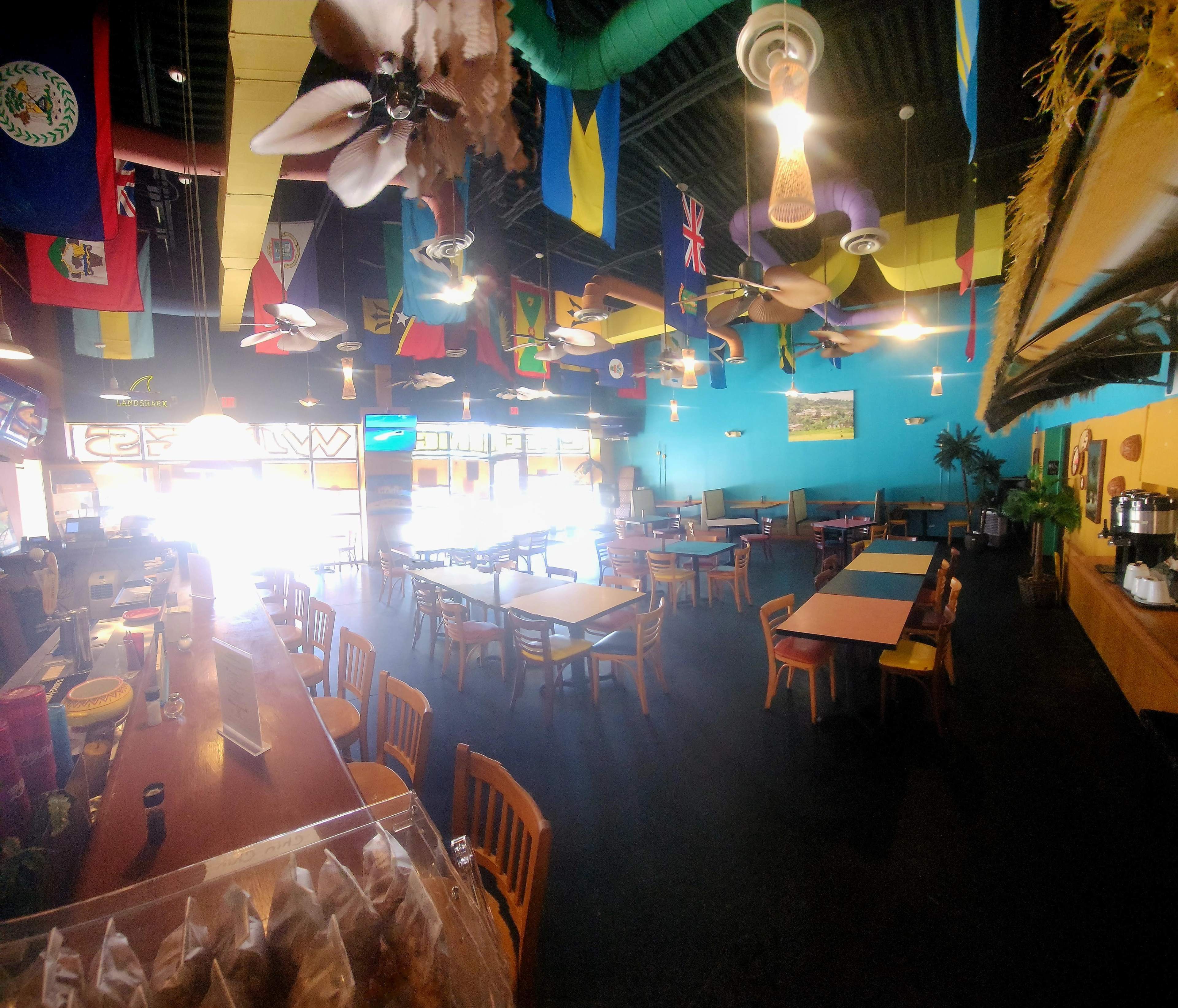 The image shows the interior of a restaurant with numerous flags hanging from the ceiling, colorful walls, and several wooden tables and chairs arranged throughout the space.