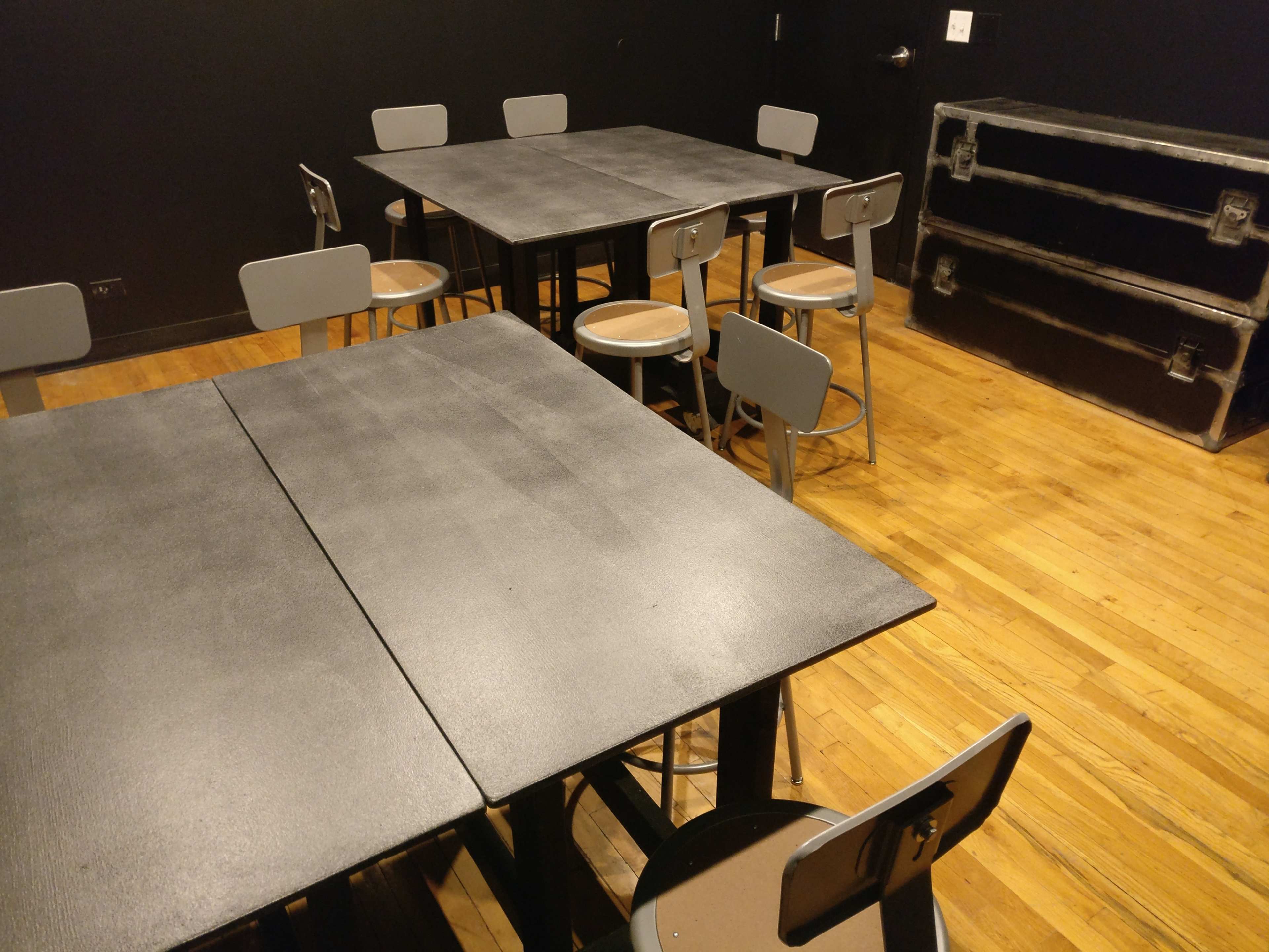 A room with several black tables and chairs arranged on a wooden floor.