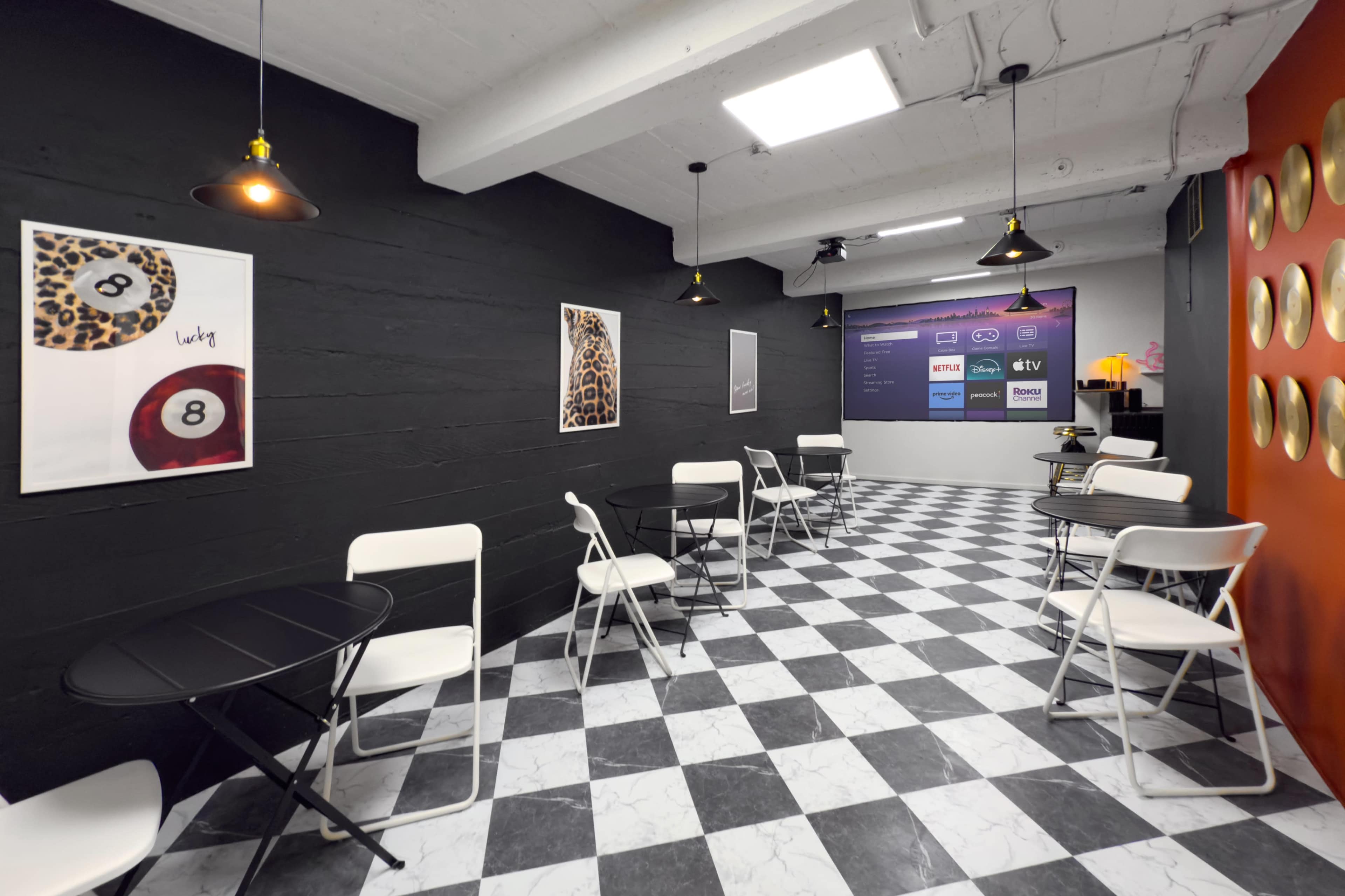 The image shows a modern cafe interior featuring black and white checkered flooring, several black tables with white chairs, and decorative wall art on a dark wall.