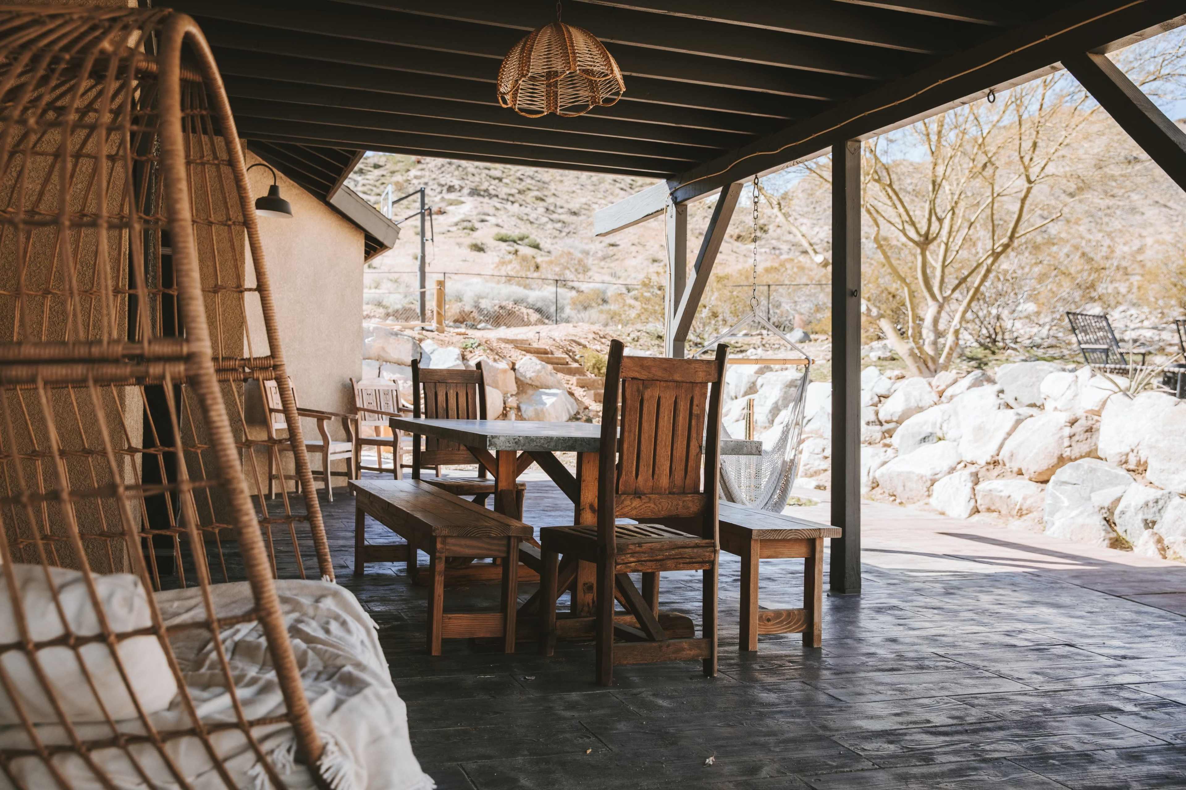 A wooden dining set with benches is placed on a covered patio overlooking a rocky landscape.