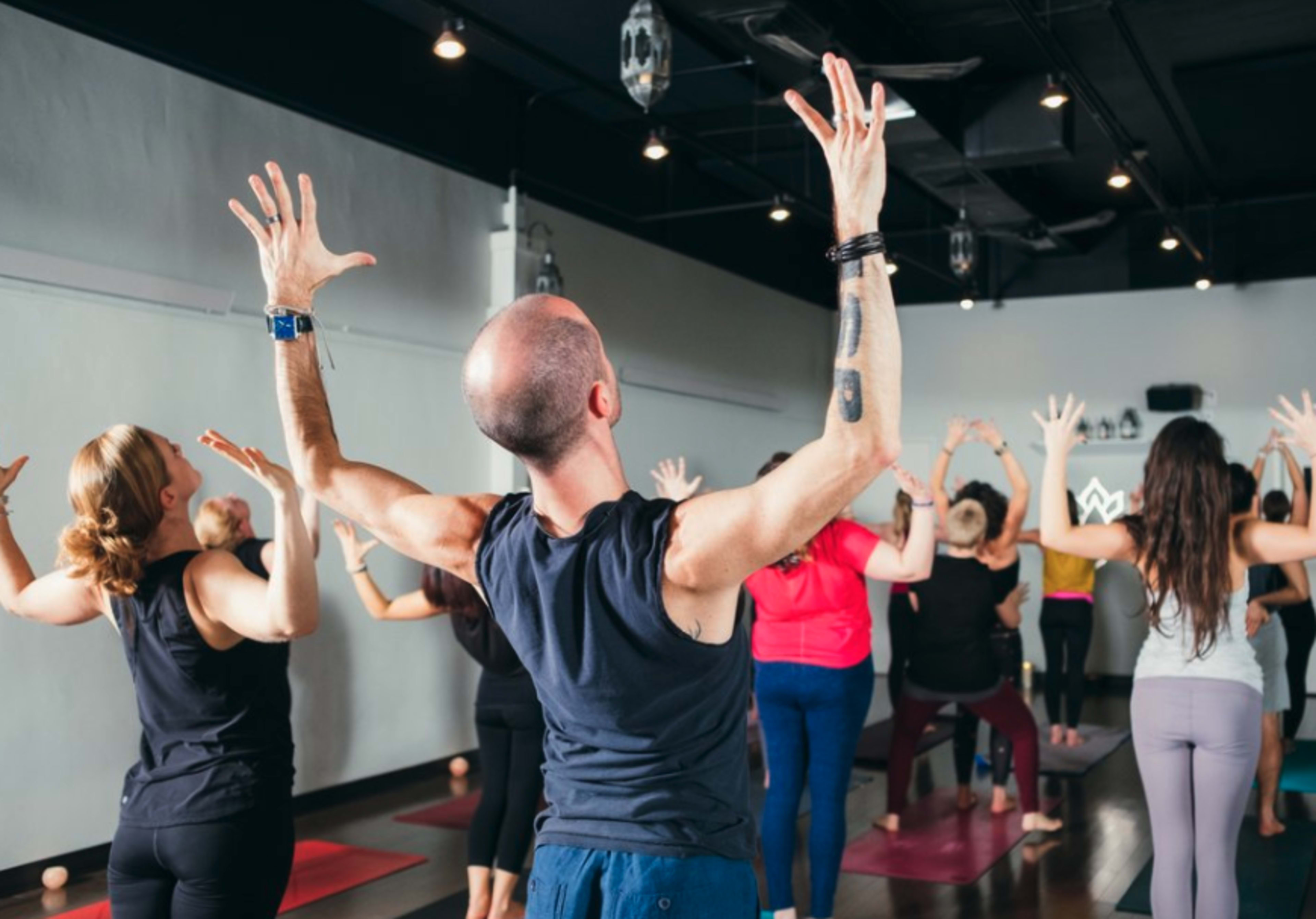 A group of people is participating in a yoga class, with various individuals positioned in different poses and raising their arms.