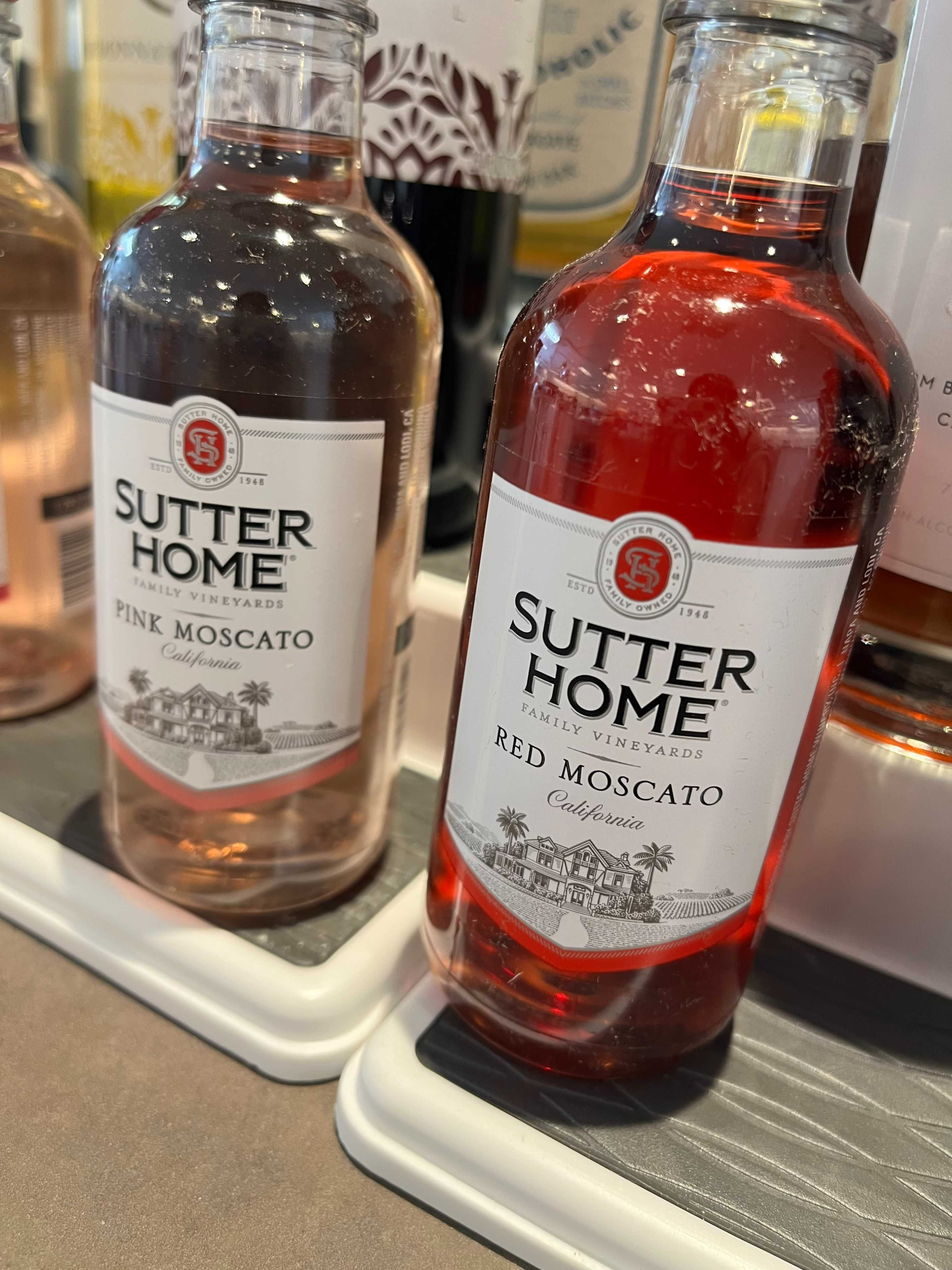 The image shows two bottles of Sutter Home wine, one labeled as Pink Moscato and the other as Red Moscato, both resting on a display surface.