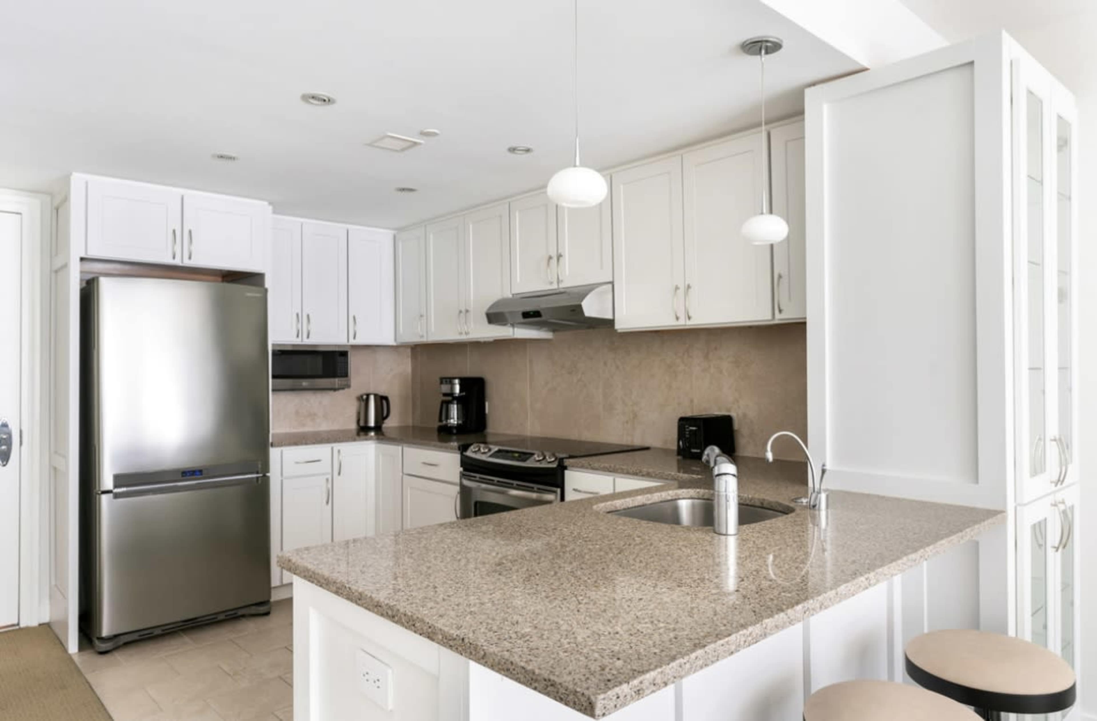 The image shows a modern kitchen with white cabinetry, a stainless steel refrigerator, and a granite countertop.