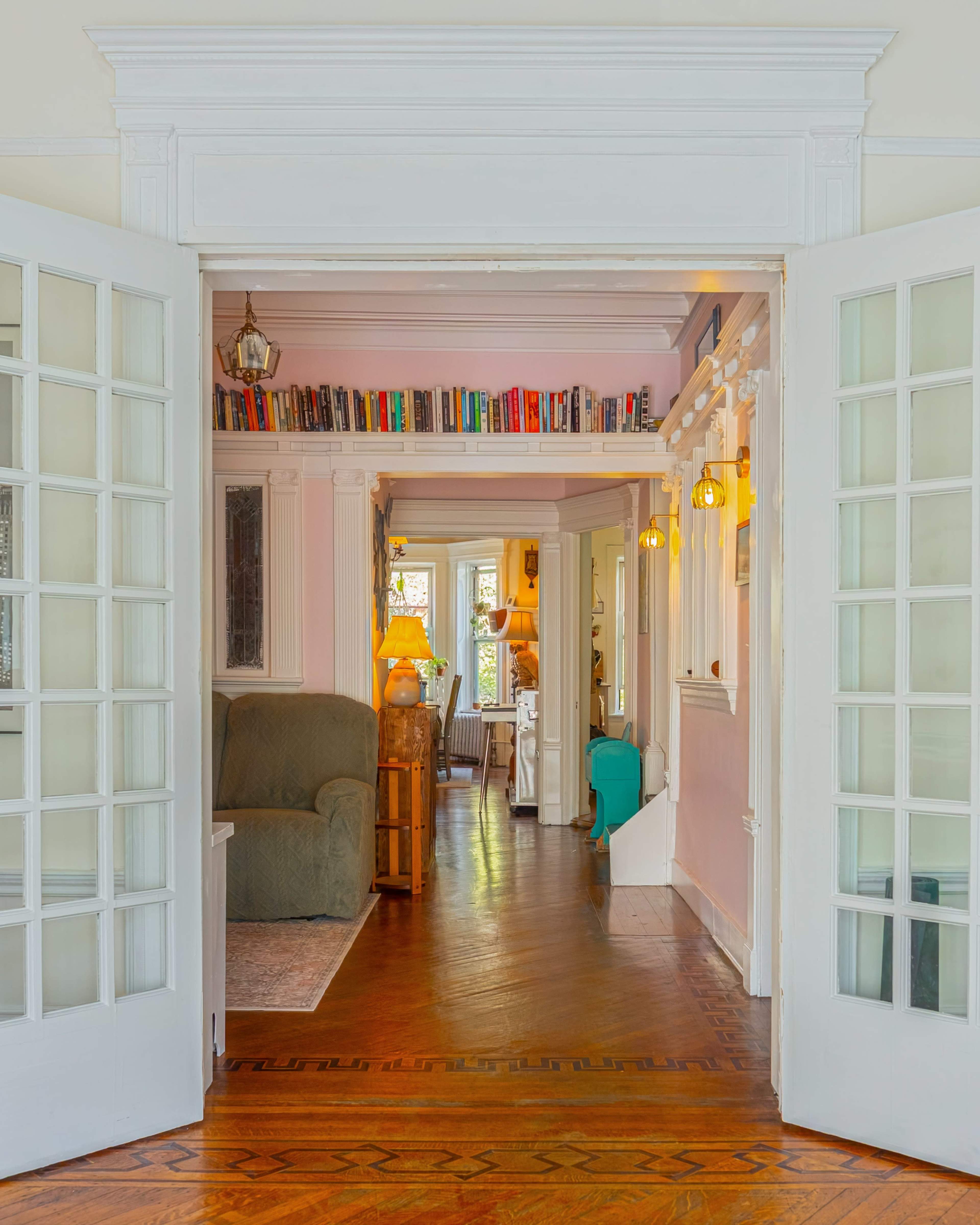 The image showcases a spacious indoor area with an open doorway leading to a warmly decorated living space featuring a green sofa, bookshelves, and light fixtures.