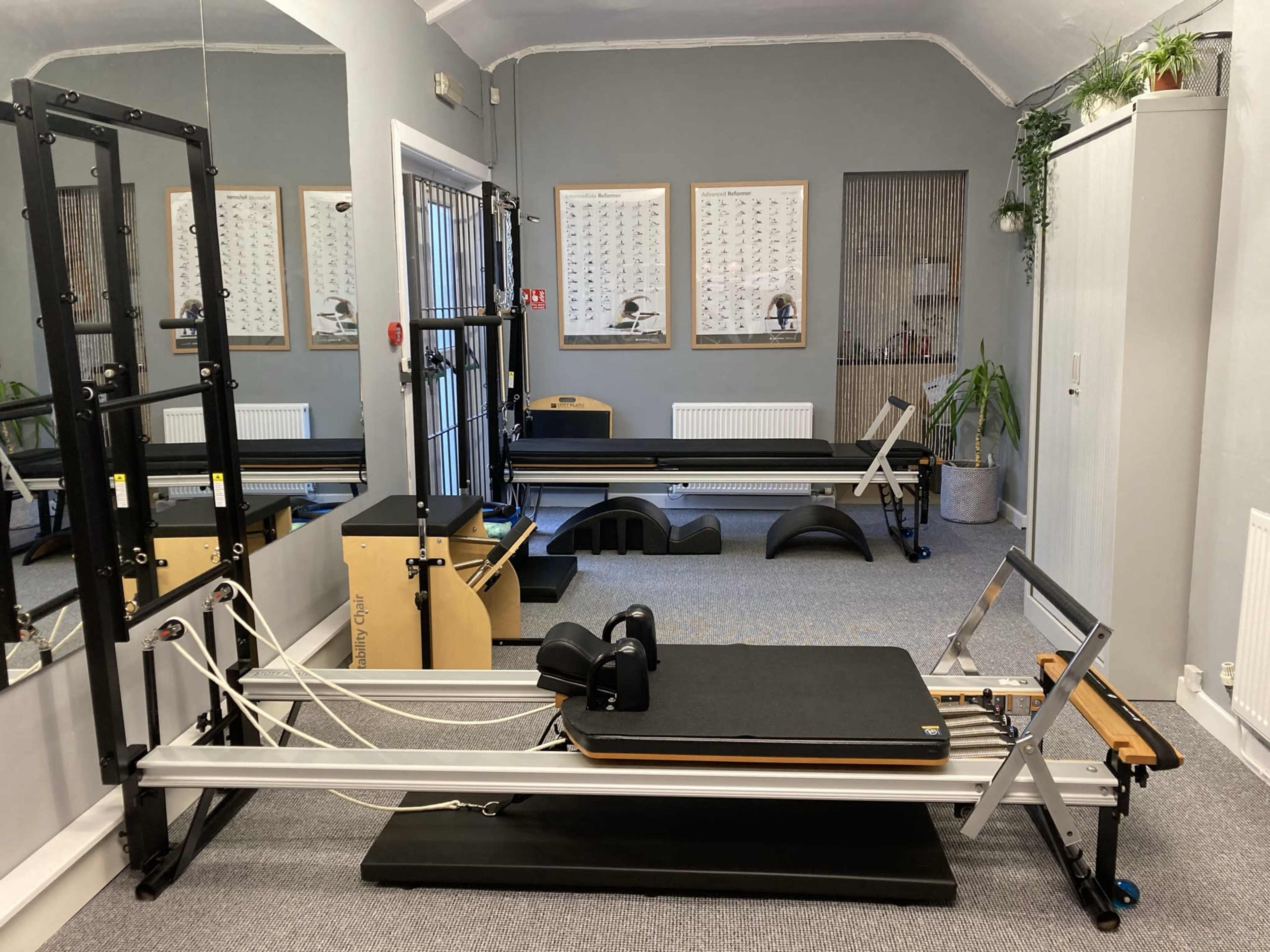 A Pilates studio featuring various equipment, including reformers and a wall unit, set against a neutral-colored wall.
