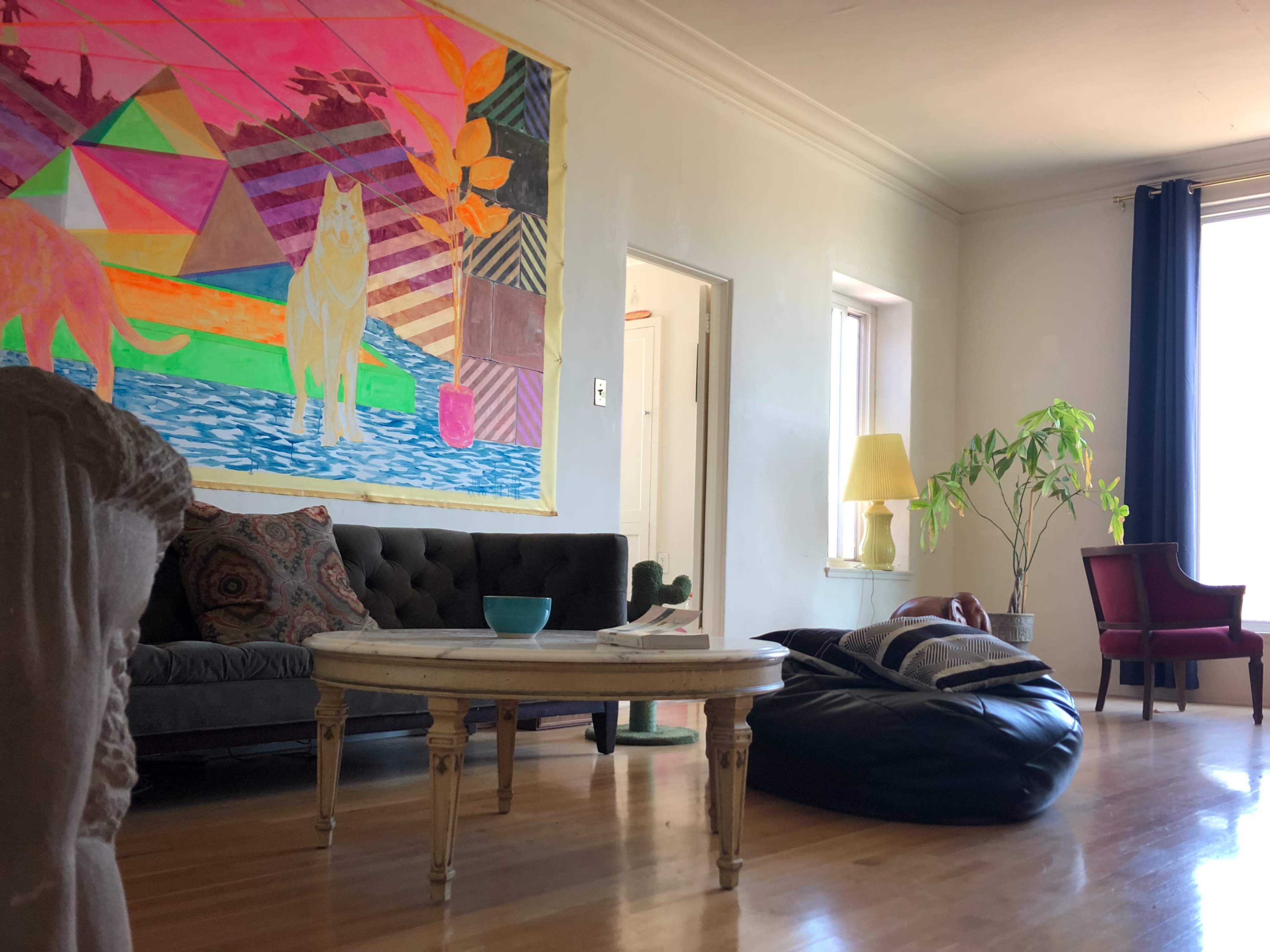 A living room with a colorful mural on one wall, a black bean bag chair, a round coffee table, and various seating options including a sofa and an armchair.