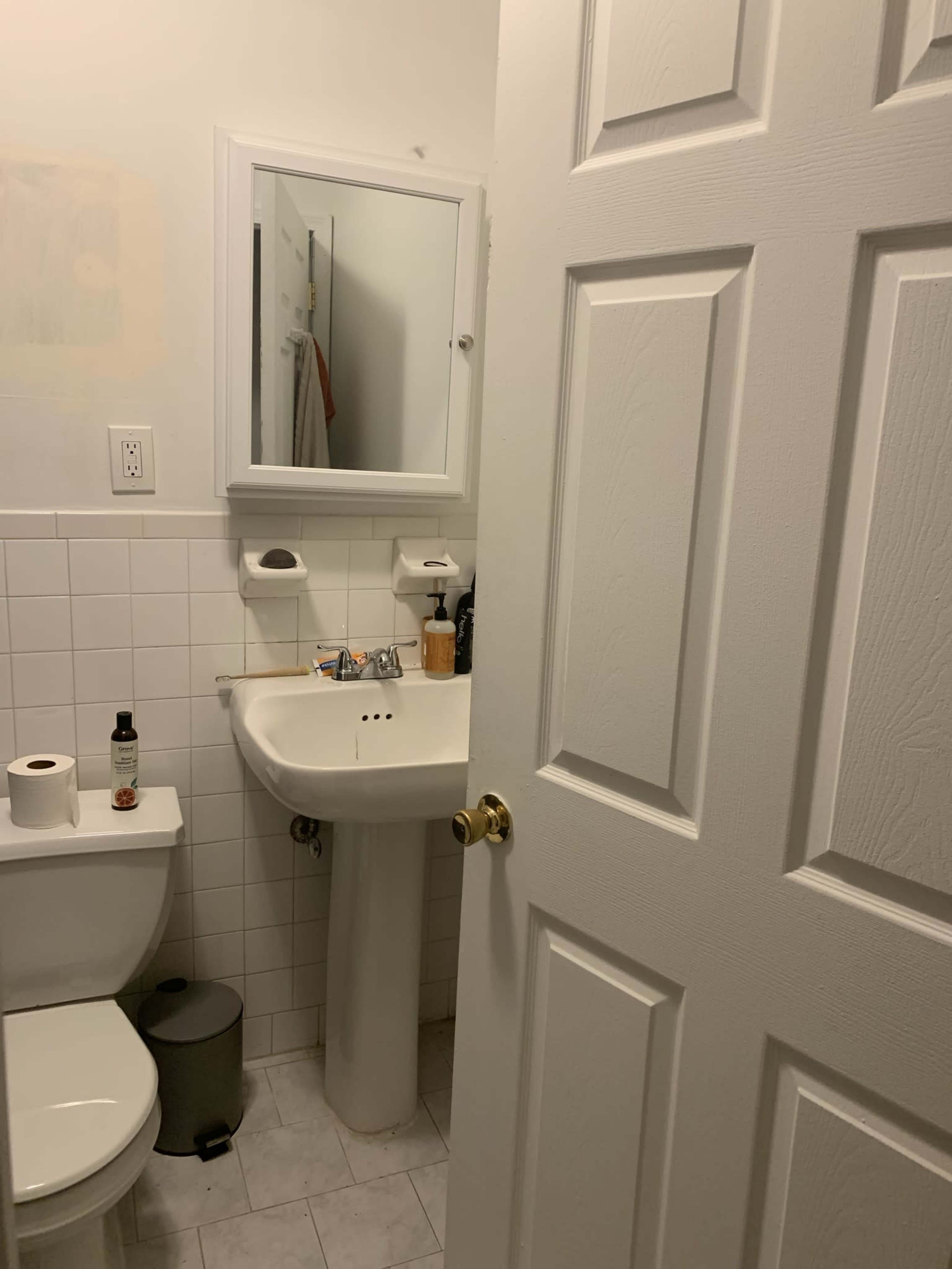 A bathroom is shown with a white tiled floor, a sink, a toilet, and a partially opened door revealing the room's contents.