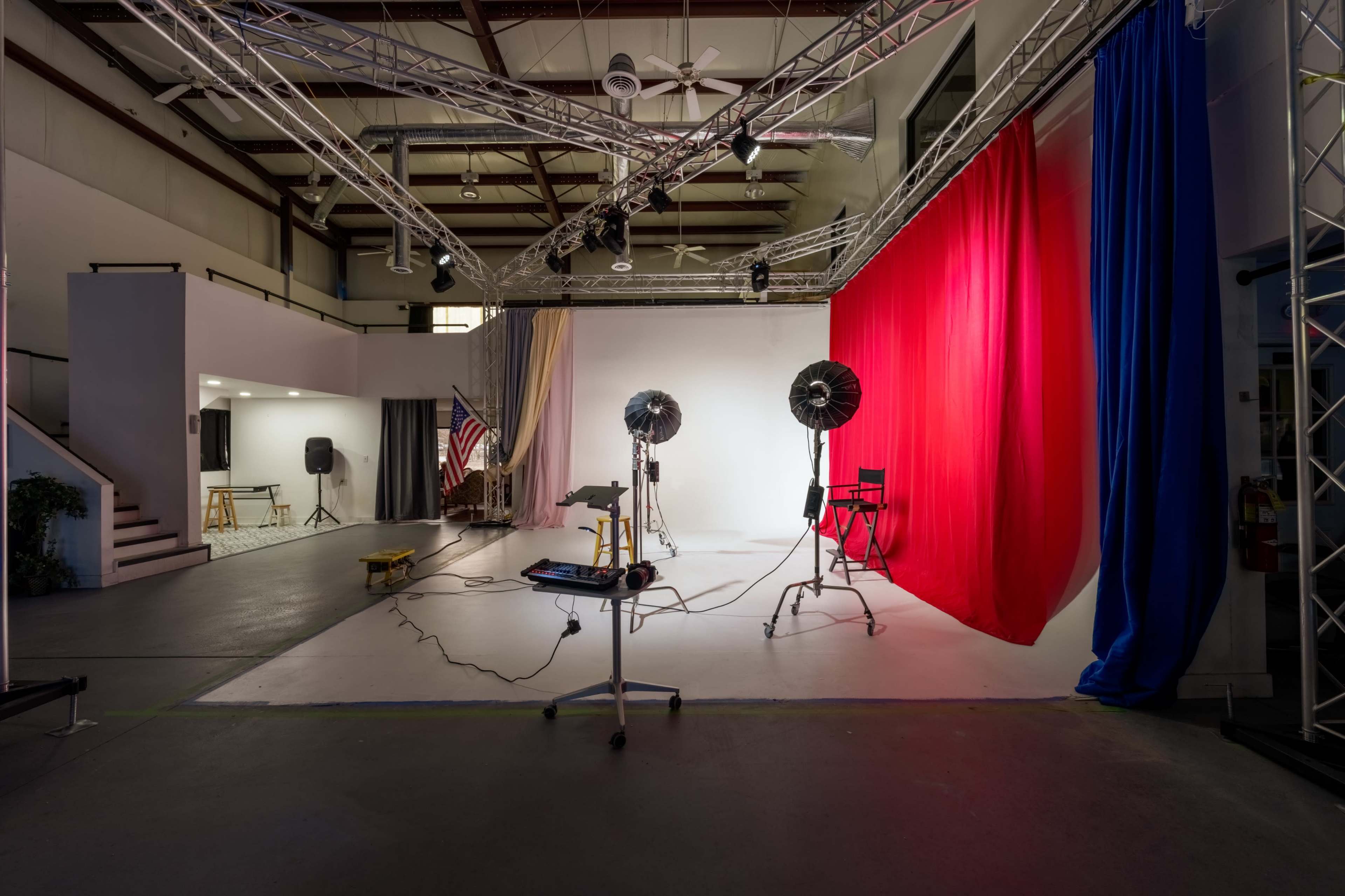 The image shows a studio space with lighting equipment, backdrop curtains in red and black, and various props arranged for a photoshoot.