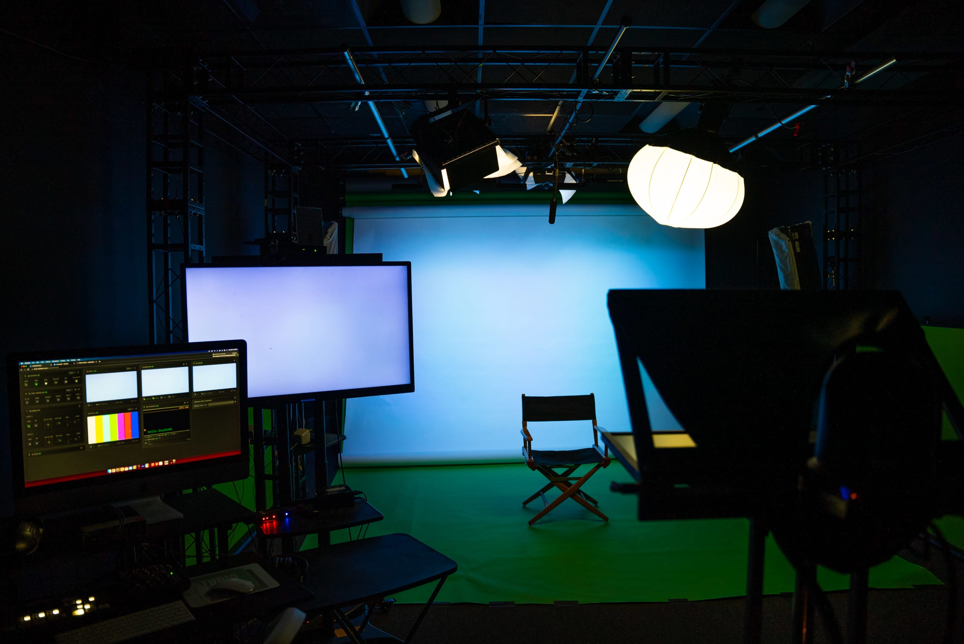A video production studio is set up with lighting, screens, and a director's chair against a green screen backdrop.