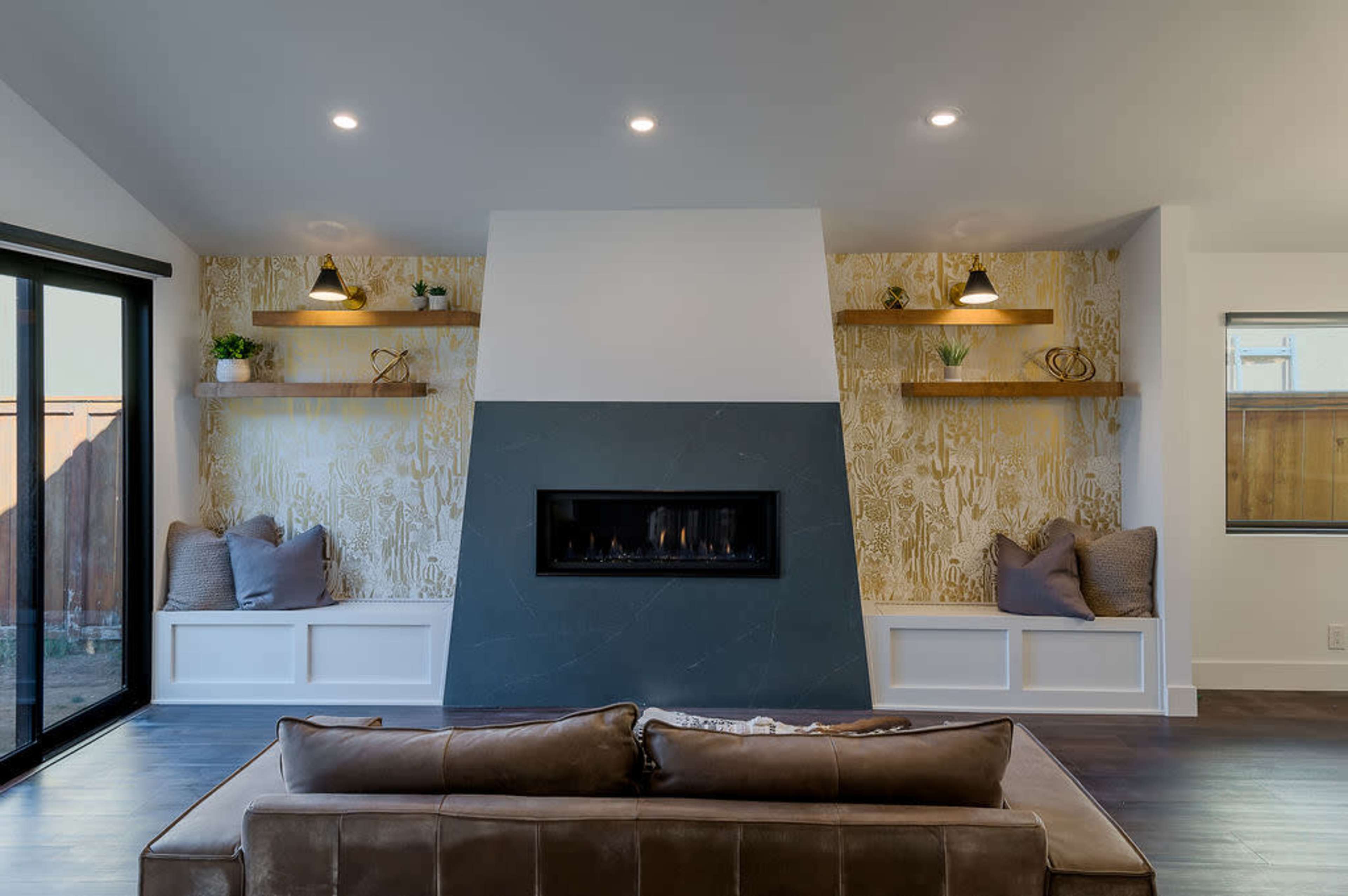 A modern living room with a central stone fireplace, two built-in seating areas, and decorative shelves against a patterned wall.