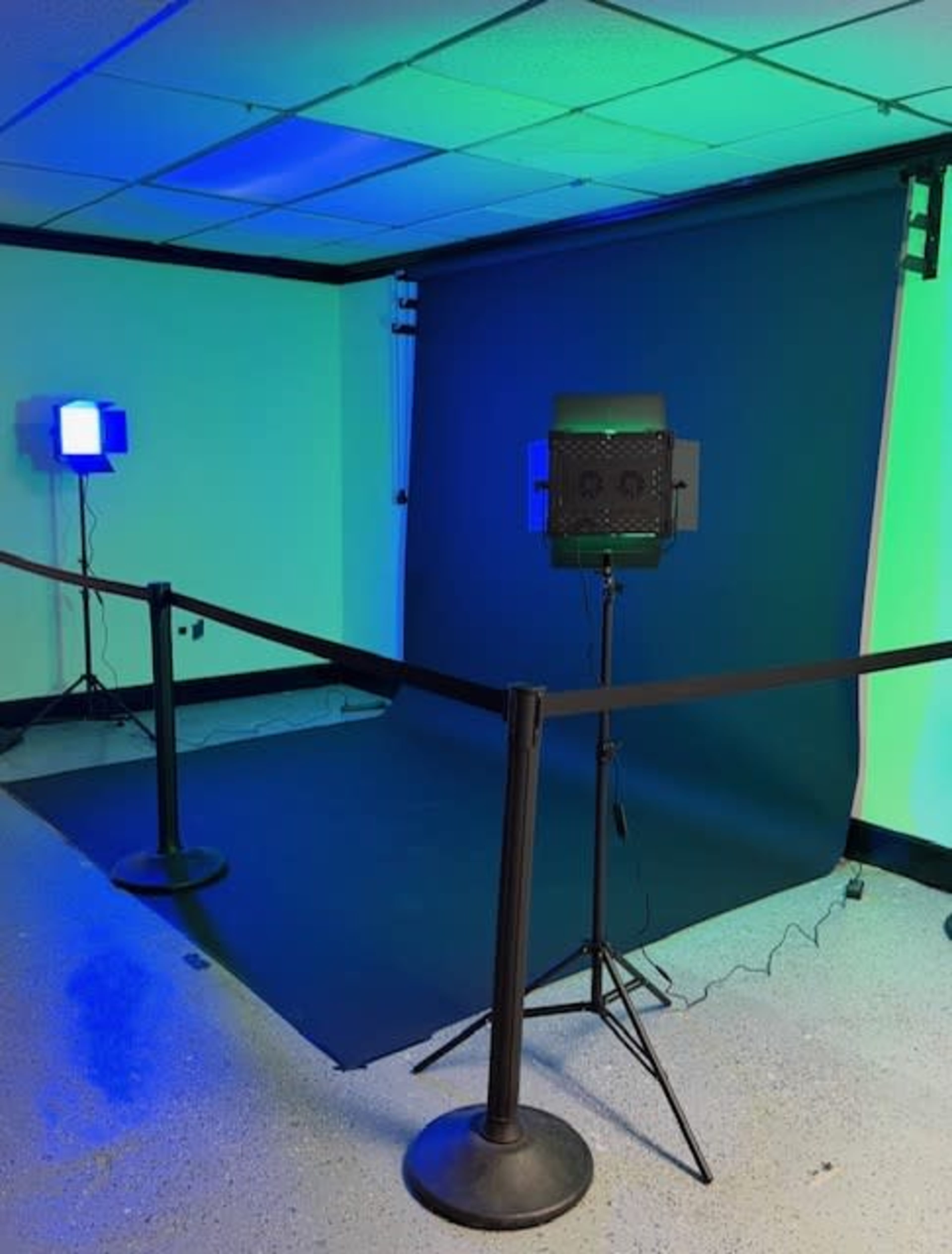 The image shows a photography setup featuring a dark backdrop, two light sources, and a barrier cord in an indoor space.