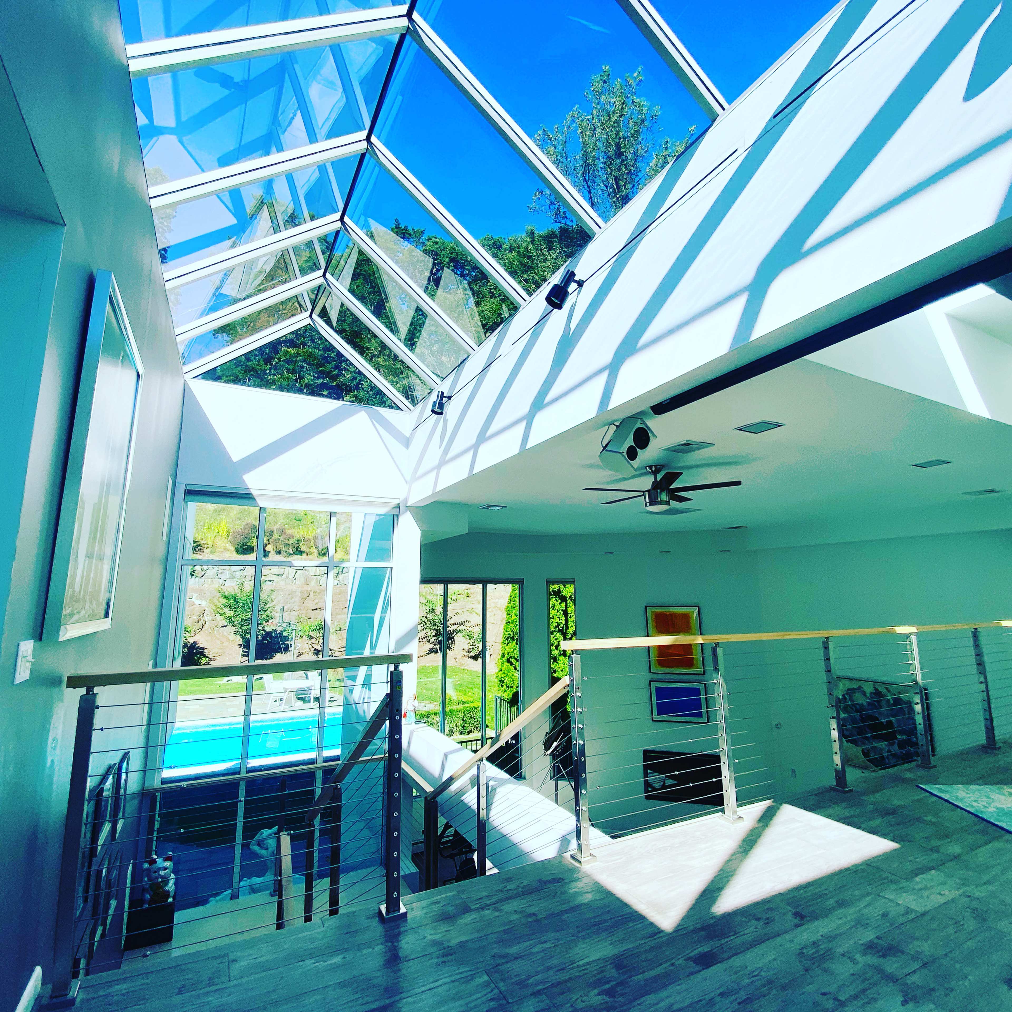 A modern, open-concept living space with large glass windows and a view of a pool and landscaped garden.