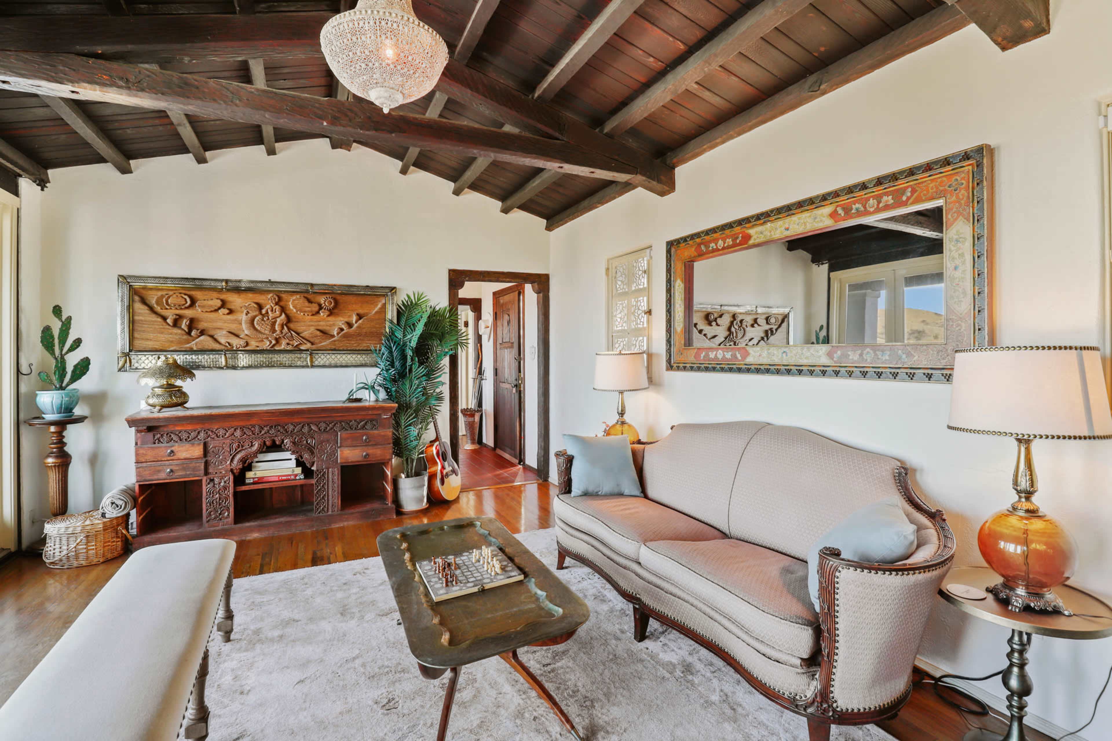 A living room with a wooden ceiling, a beige sofa, a decorative console table, and two framed mirrors on the walls.