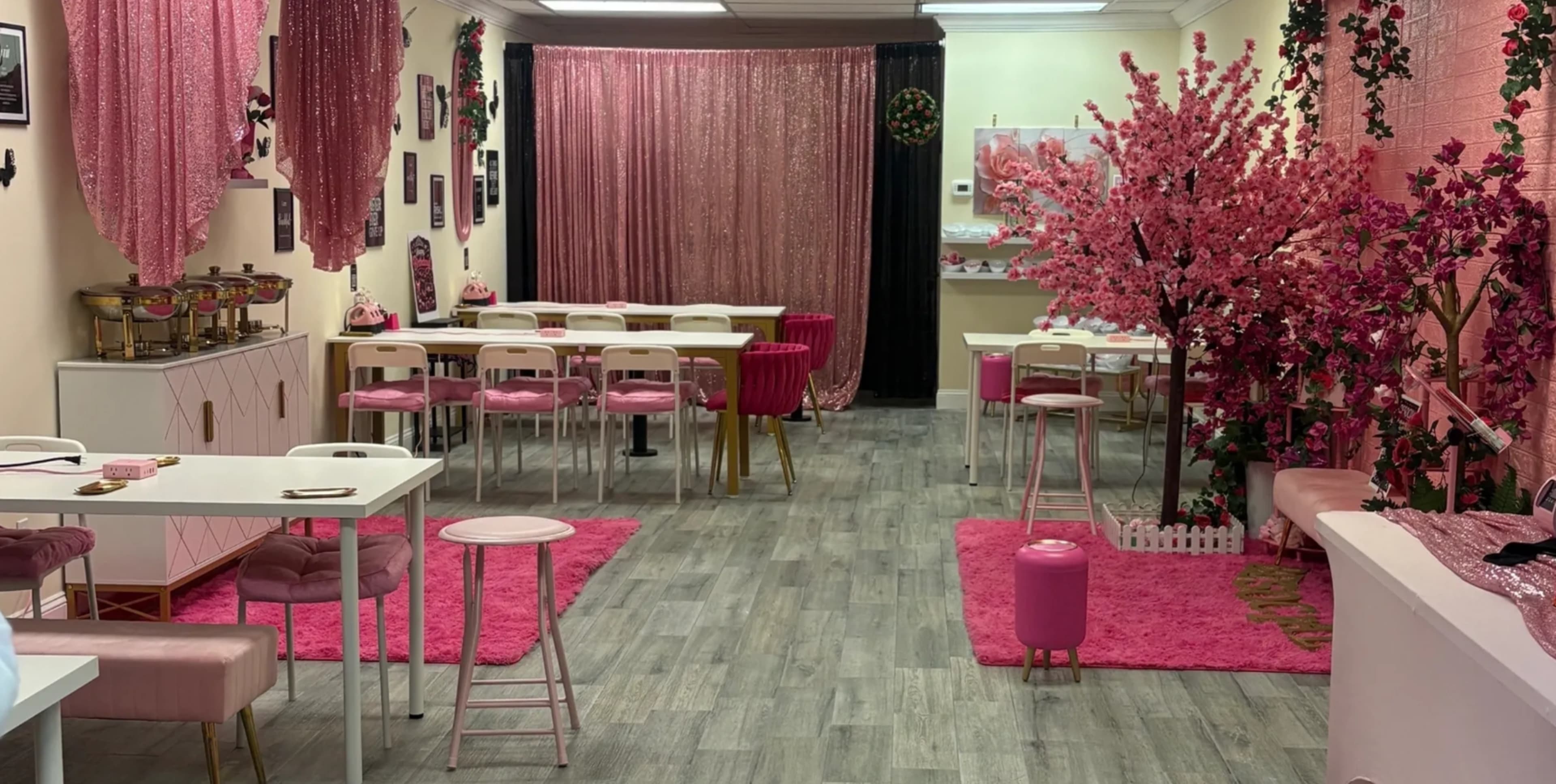 The image features a pink-themed café interior with tables and chairs arranged around a central decorative pink tree and carpet.
