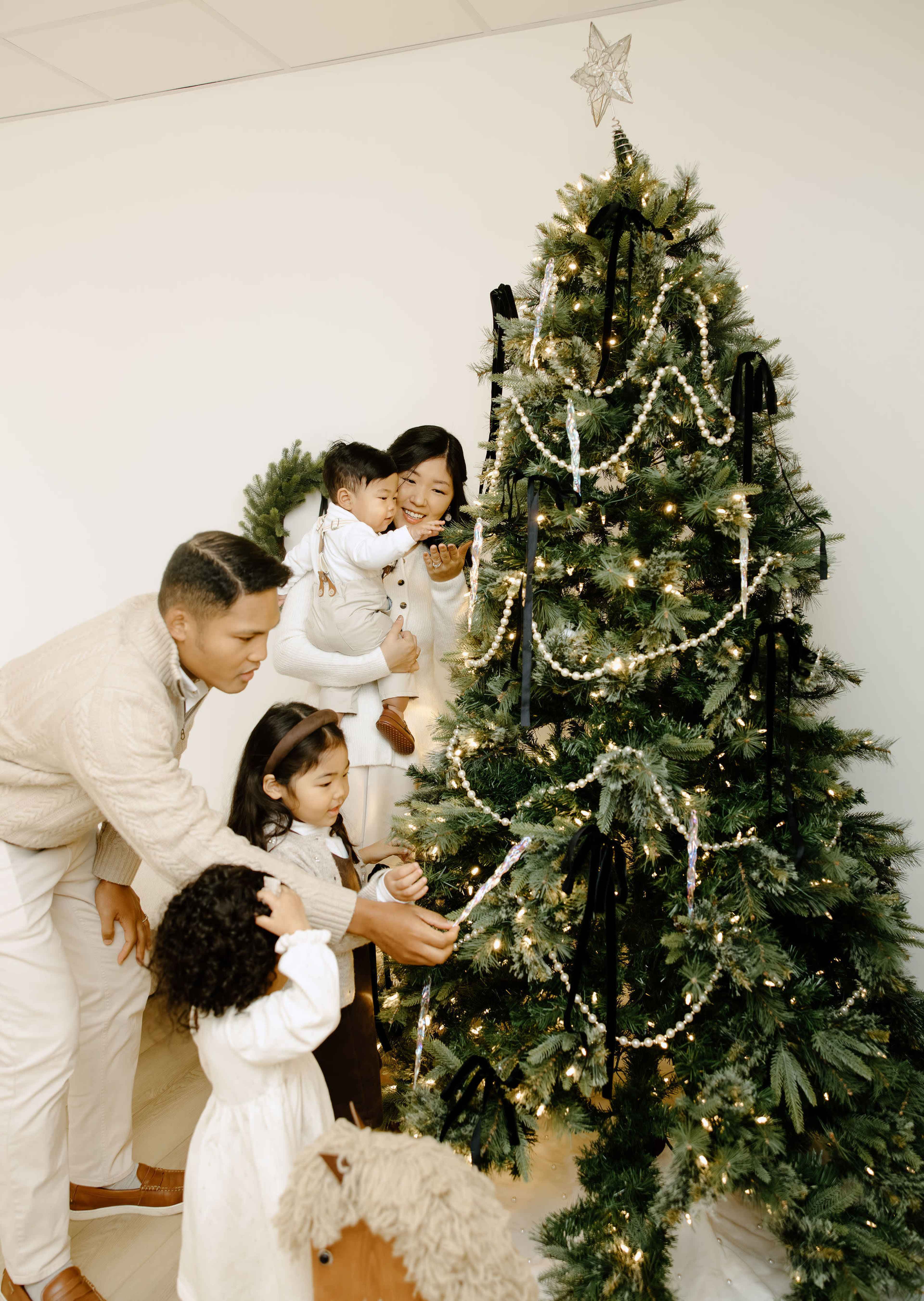 A family gathers around a decorated Christmas tree adorned with lights and ornaments.