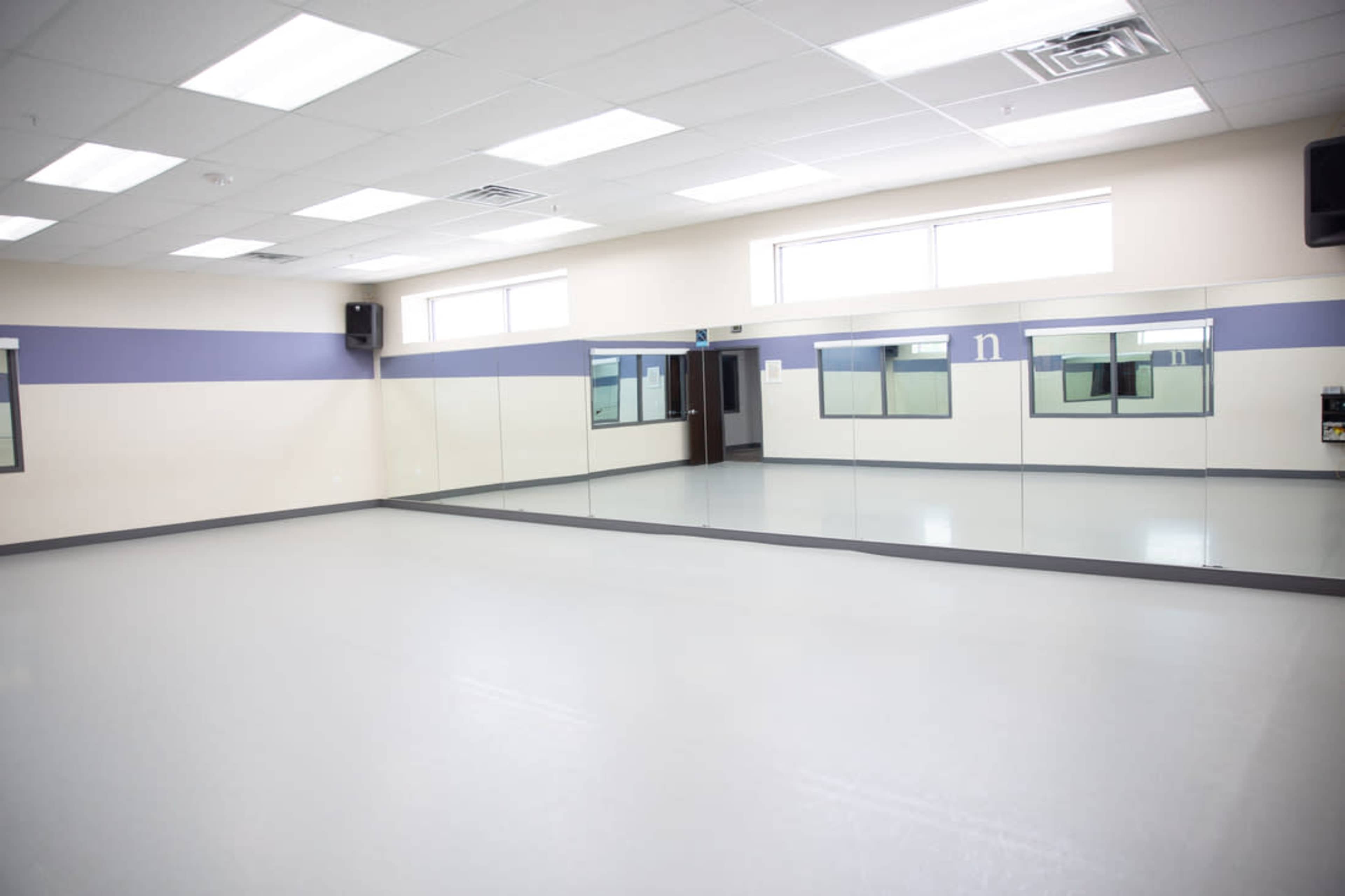 A bright, empty studio space with large mirrors along one wall and a smooth gray floor.