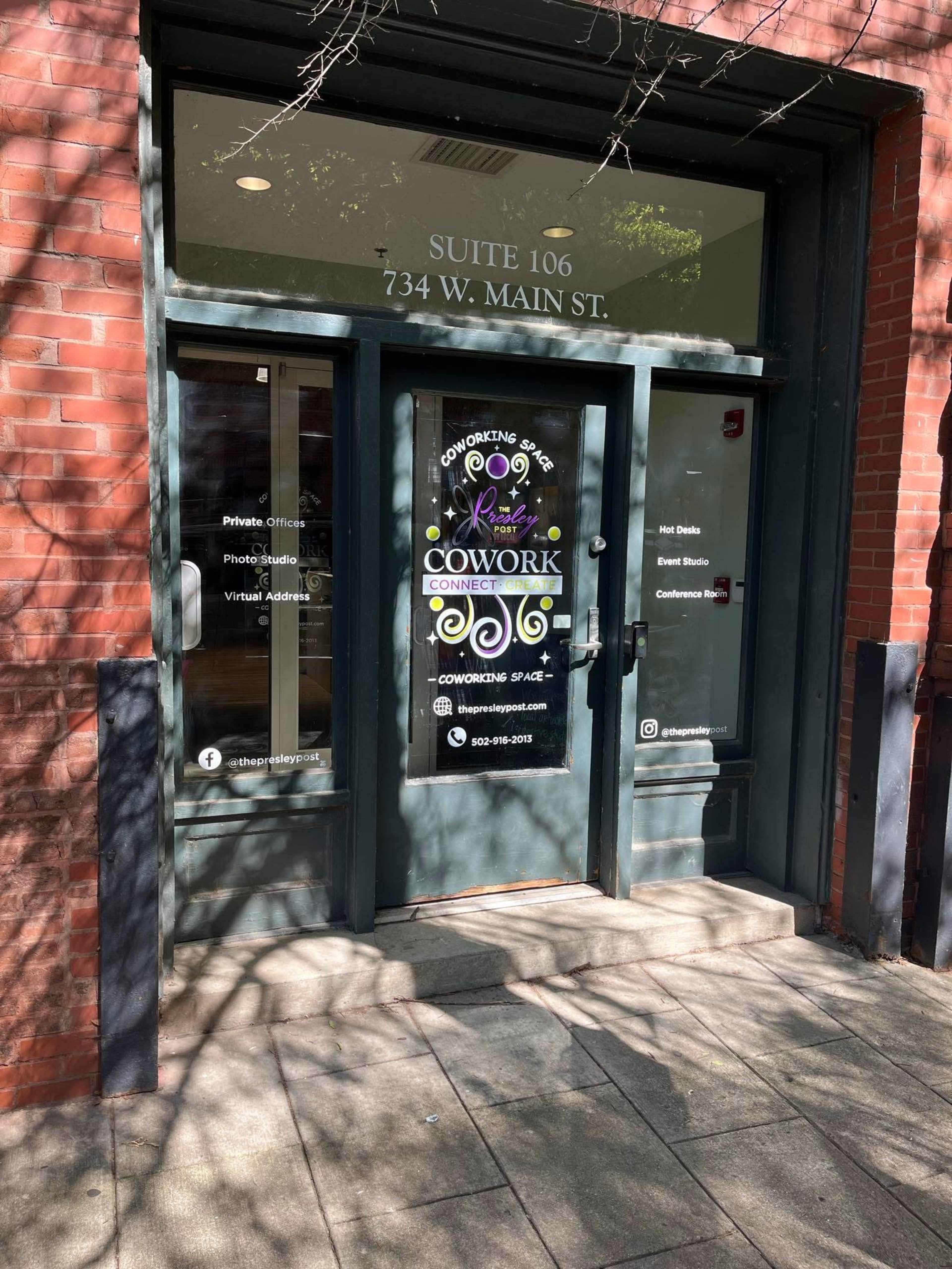 The image shows the entrance to a coworking space, featuring a glass door with signage that includes the address "734 W. Main St." and information about services offered.