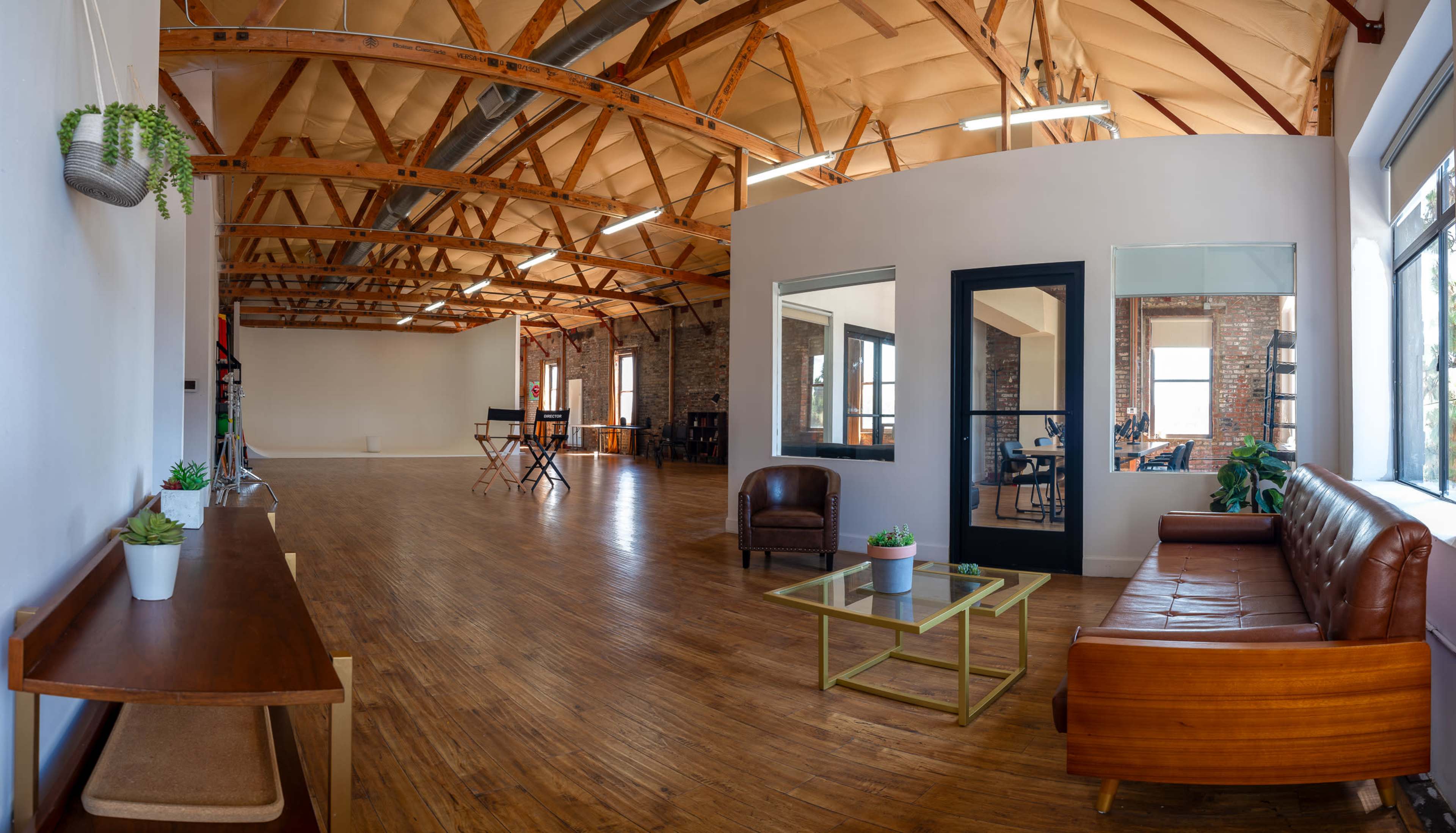 A spacious, well-lit room with wooden floors, exposed beams, and a lounge area furnished with a leather sofa and glass coffee table.