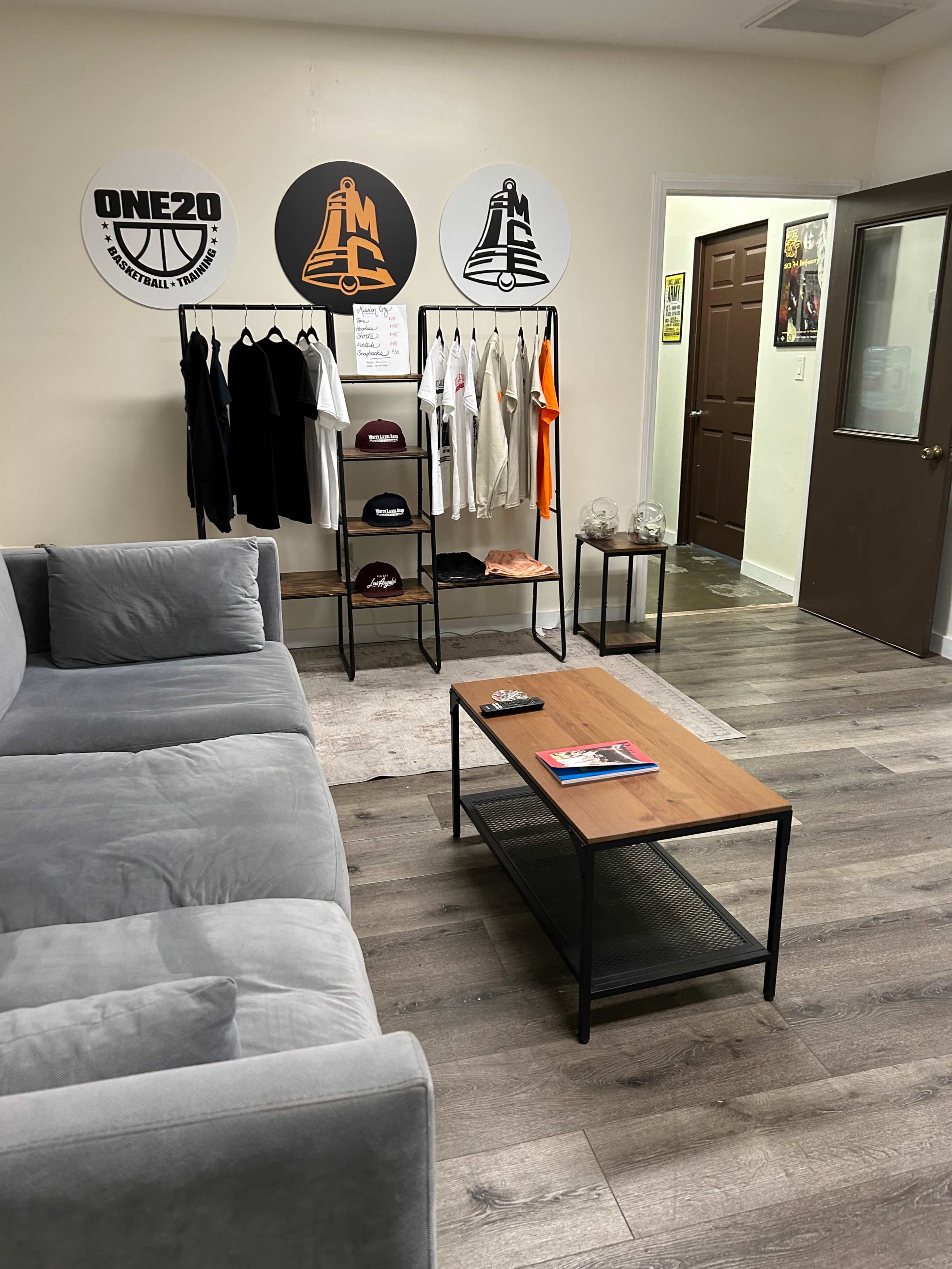 The image shows a modern room featuring a gray couch, a clothing rack displaying various apparel, and a wooden coffee table.