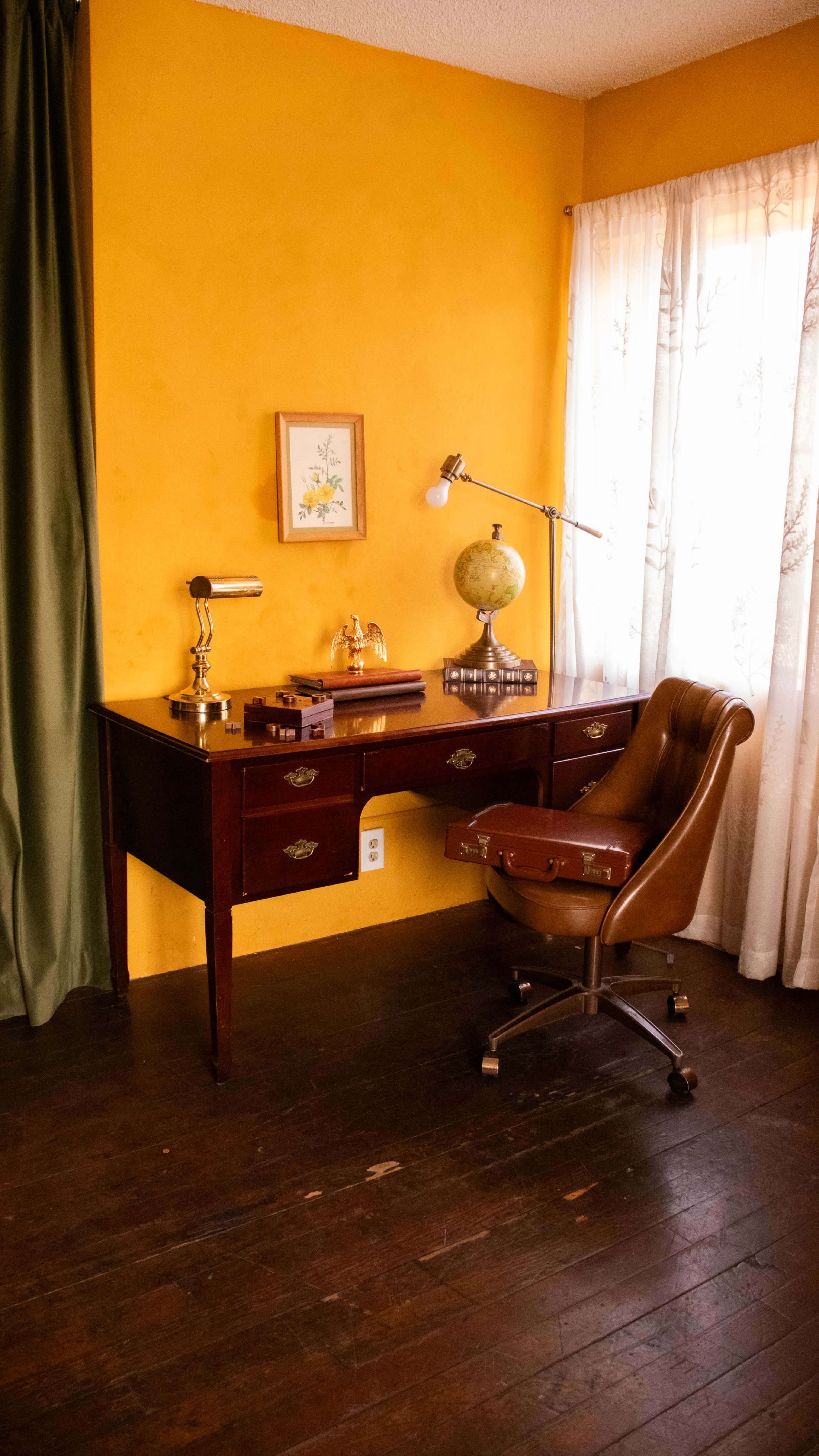 The image shows a wooden office desk with a brass lamp, a globe, and a leather chair, set against a bright yellow wall.