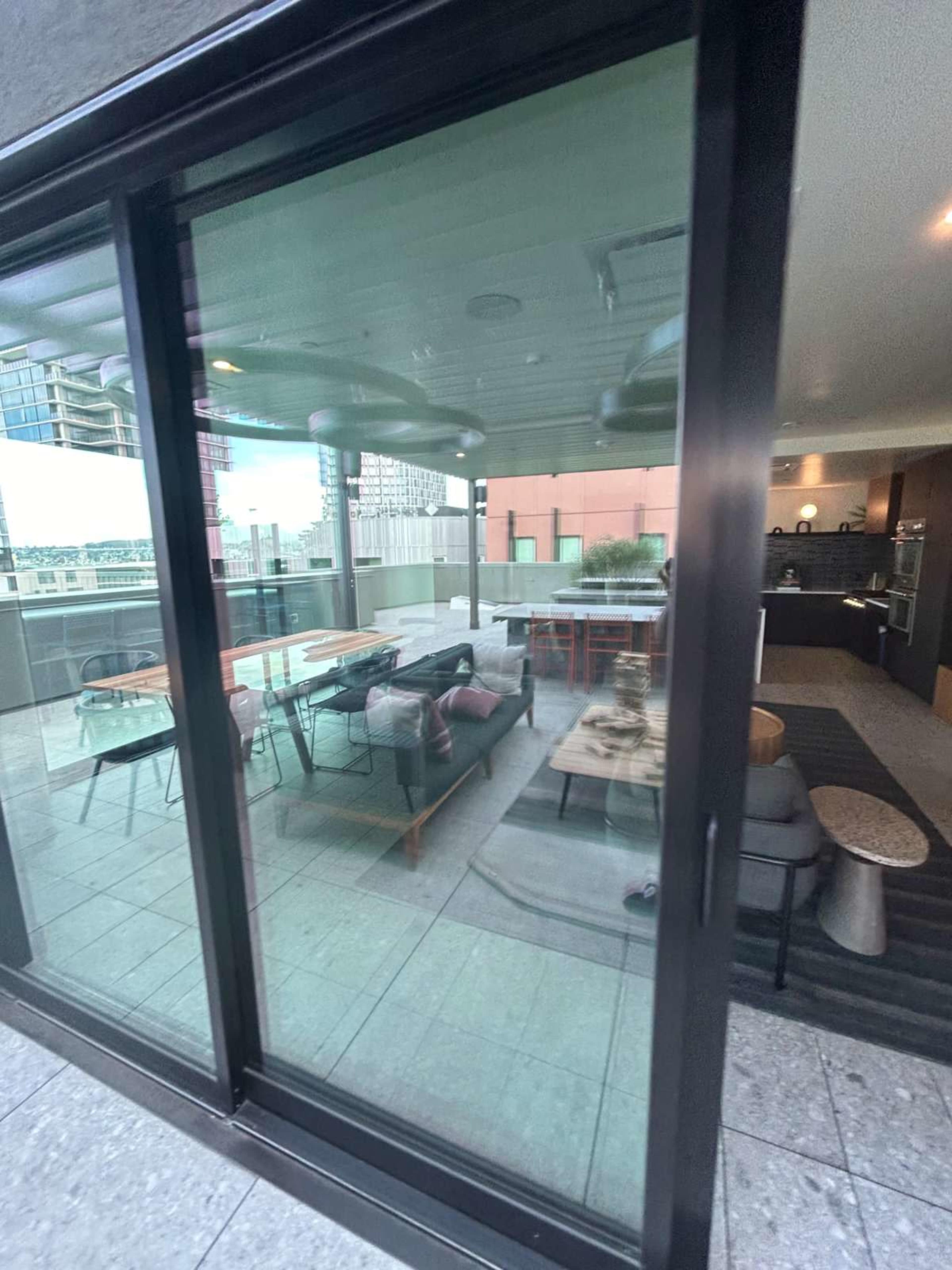 The image shows a balcony area with seating and tables, visible through a large glass window.