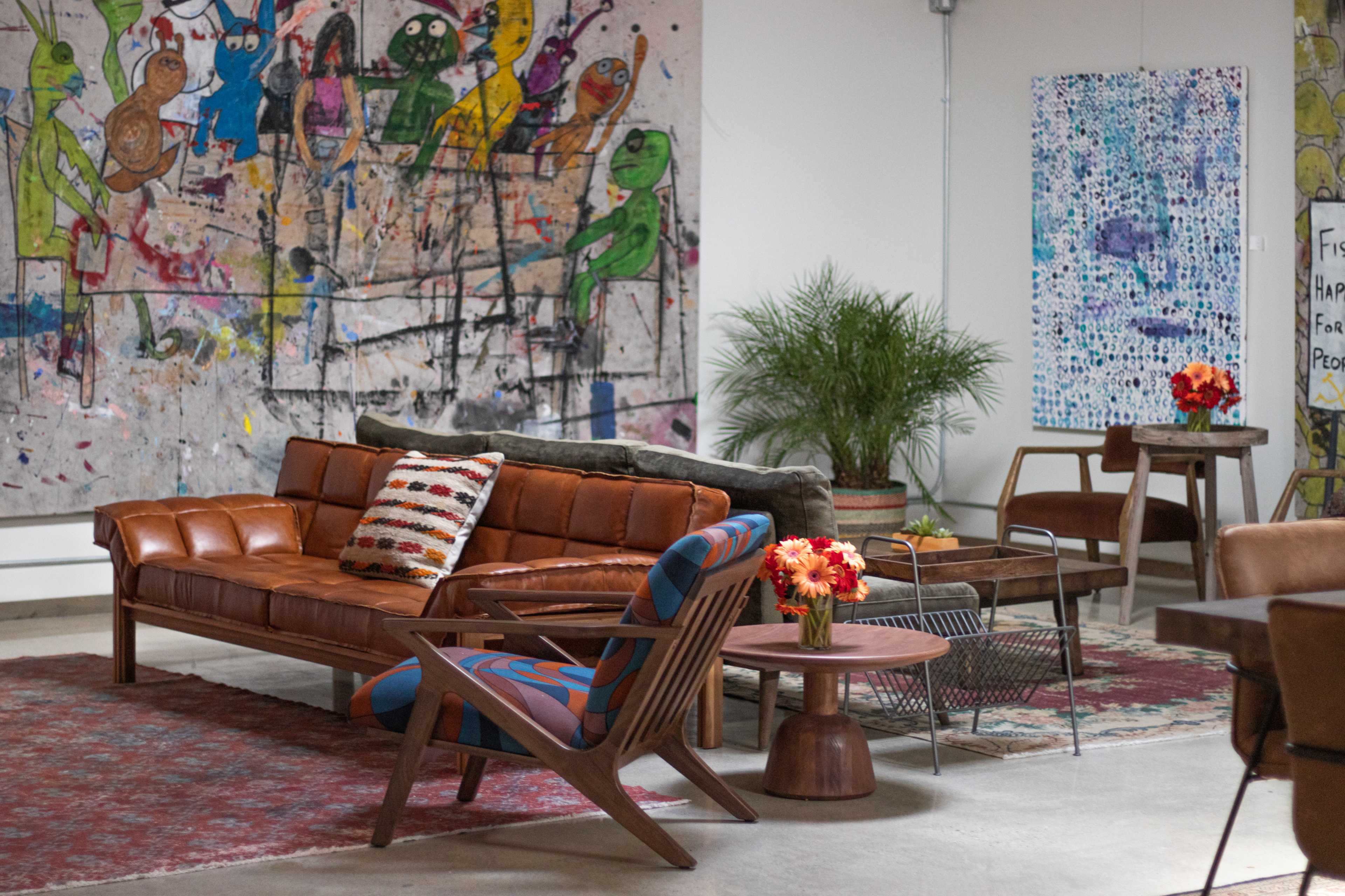 The image shows a modern interior space featuring a brown sofa, a patterned armchair, a wooden table, and colorful artwork on the walls.