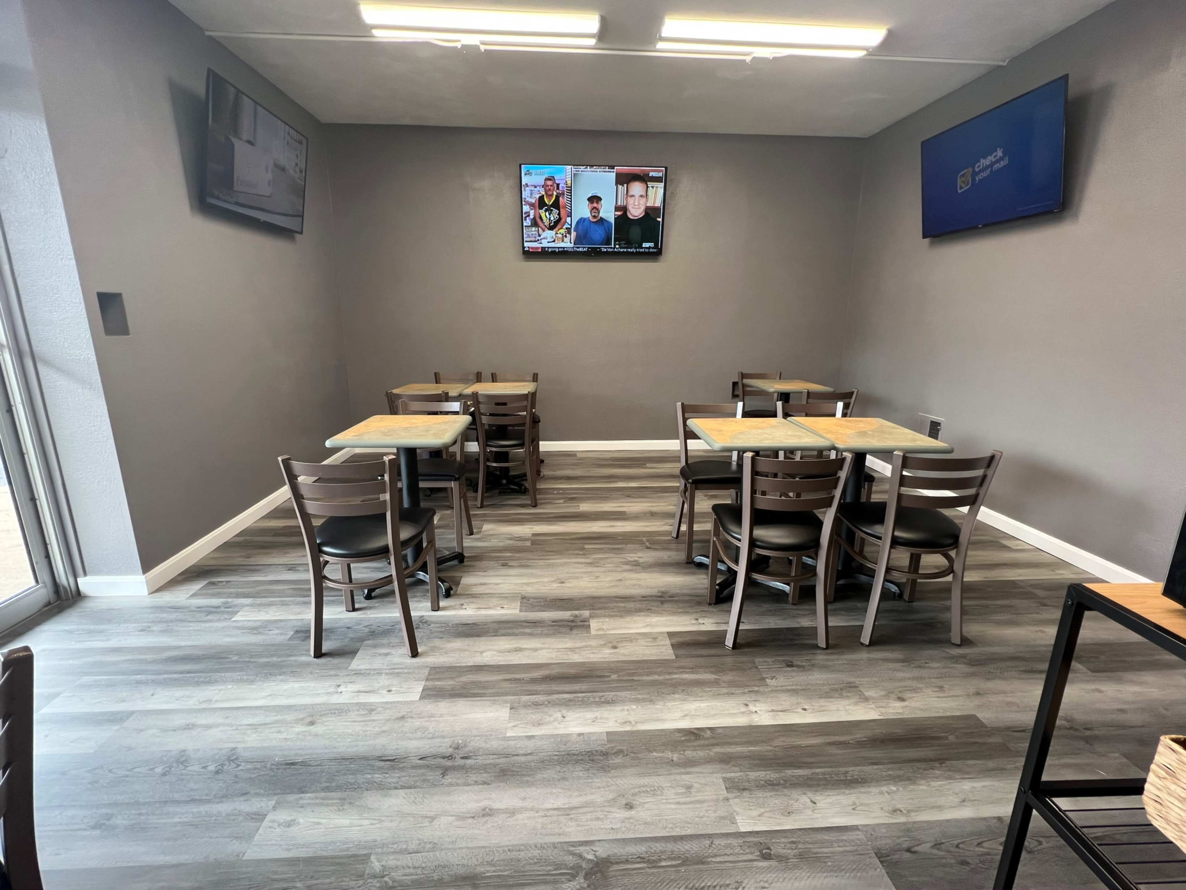 A small dining area with several wooden tables and chairs, along with two wall-mounted television screens.