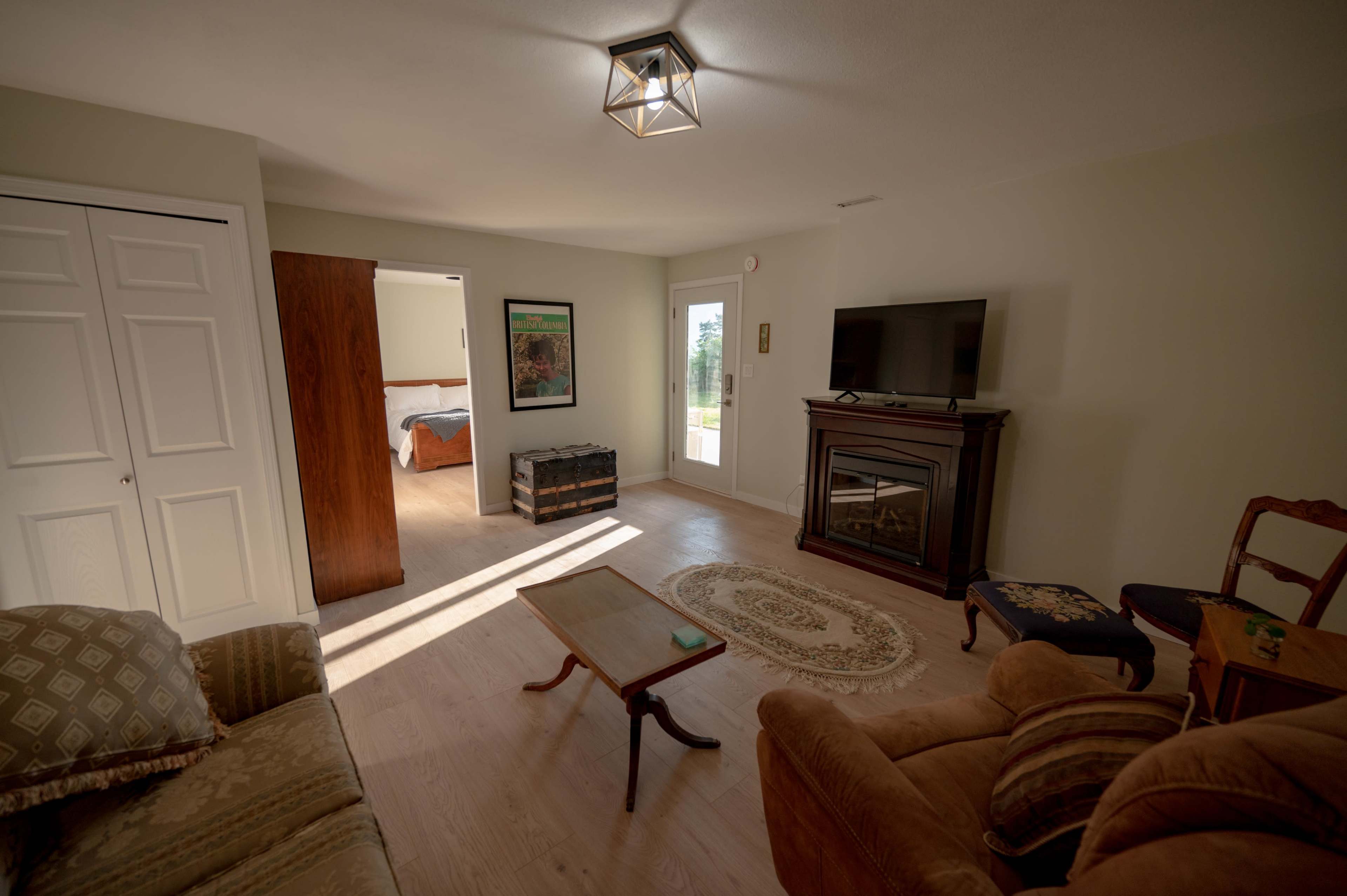 The image shows a living room with a sofa, a coffee table, a television on a stand, and a small fireplace, with a doorway leading to another room in the background.
